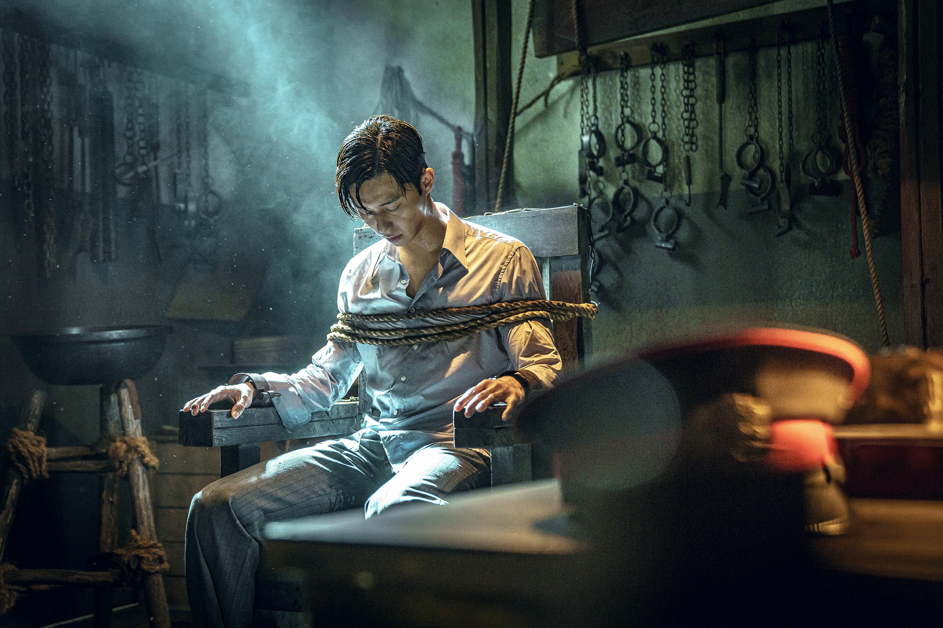 Jang Tae-sang (Park Seo-joon) sits tied to a chair in a smoky scene.