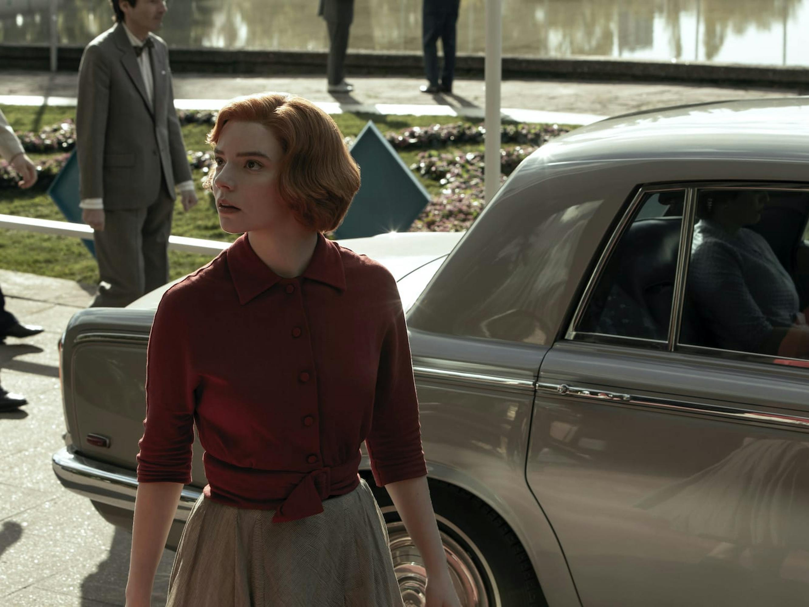 Beth Harmon wears a red blouse, and stands beside a grey car.