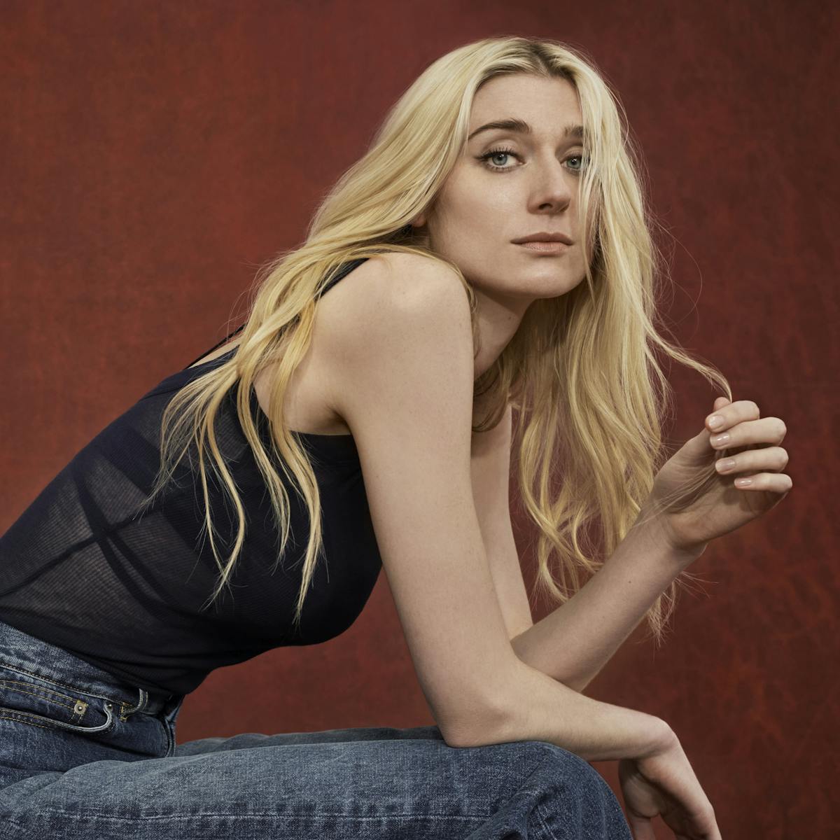Elizabeth Debicki wears a black tank top and jeans and fiddles with her long blond hair. 