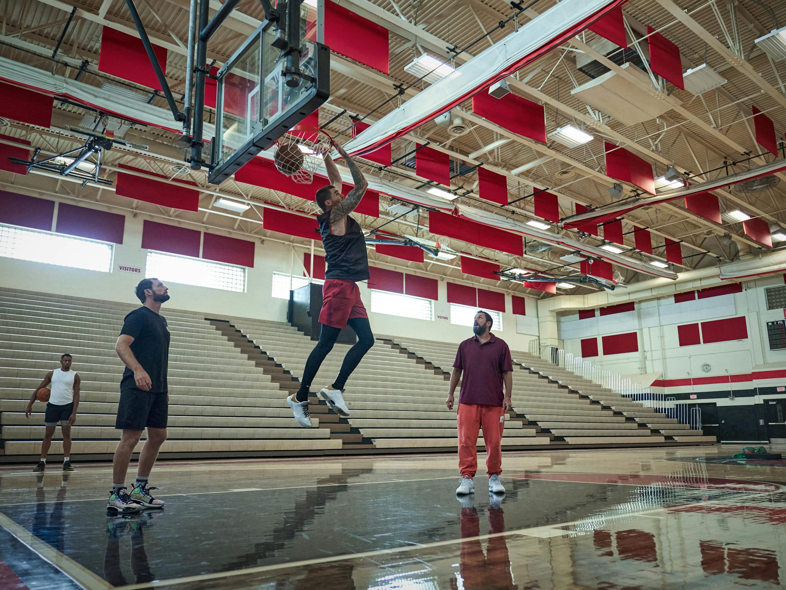 Juancho Hernangómez and Adam Sandler play basketball with some other people in a sunlit red and white gym.