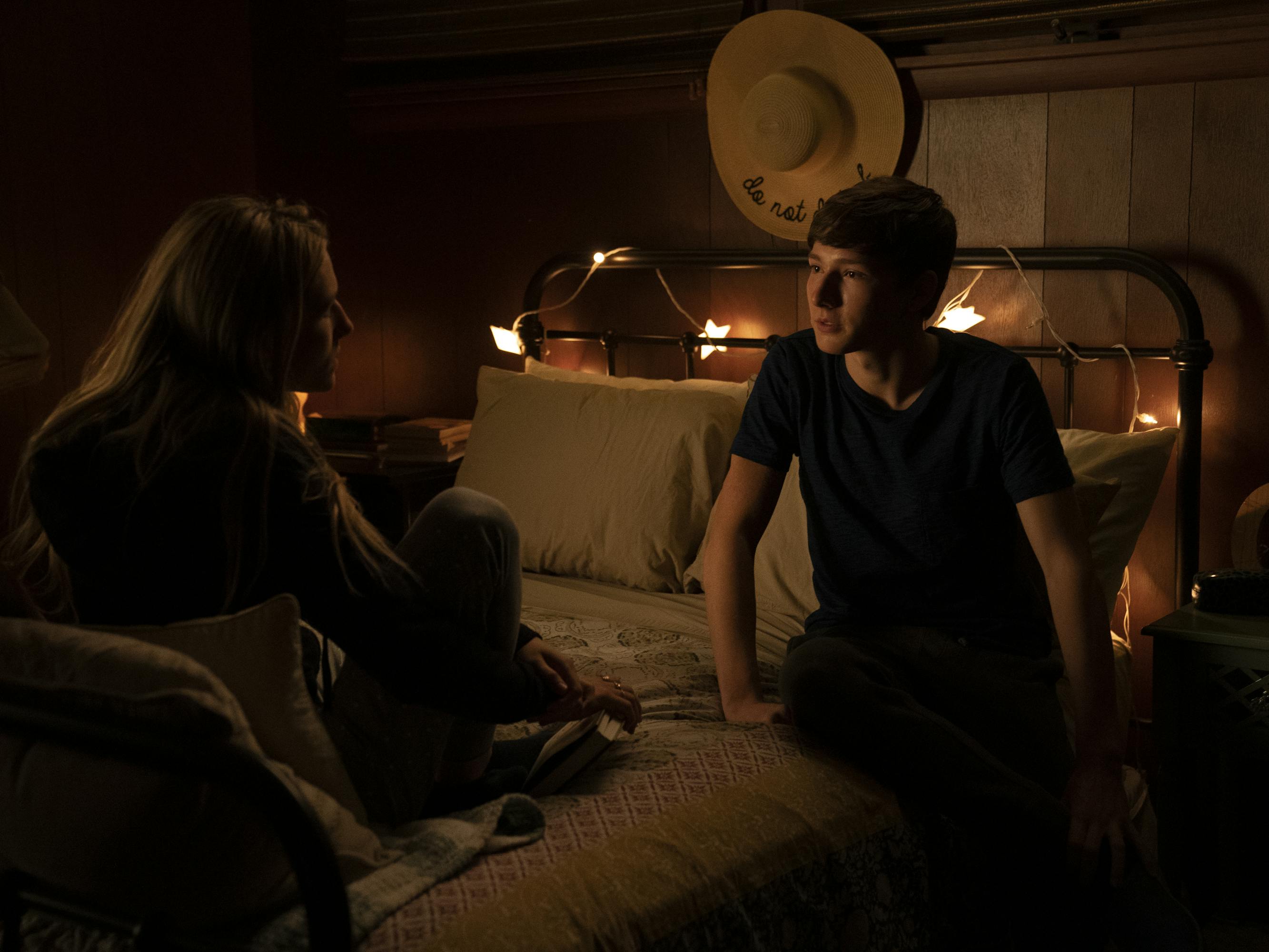 Sofia Hublitz and Skylar Gaertner sit on a bed lit by string lights.