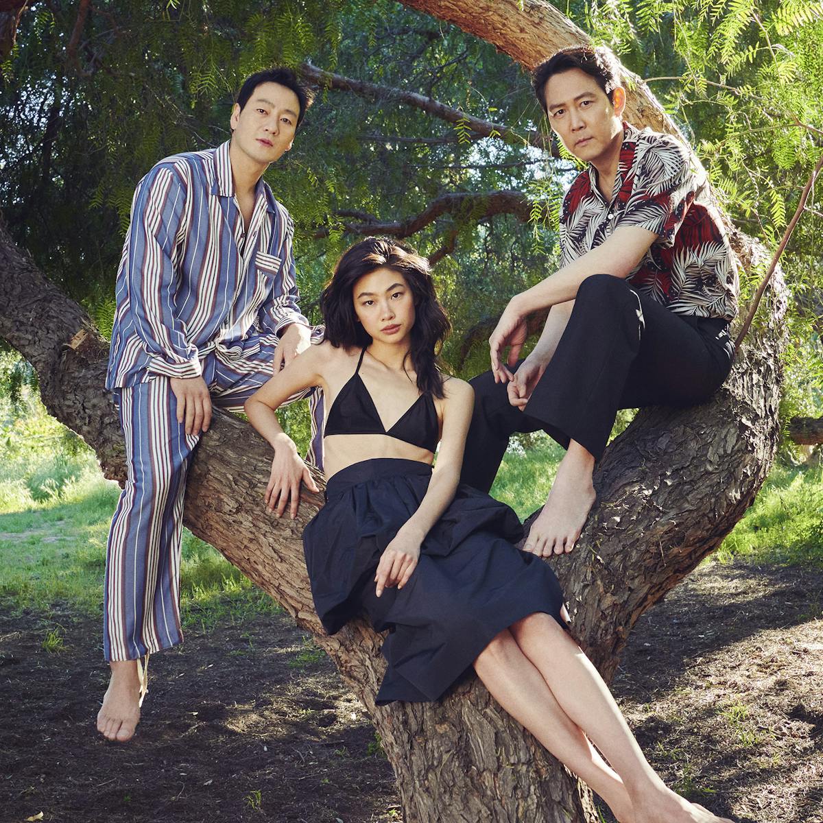 Park Hae-soo, Jung Ho-yeon, and Lee Jung-jae sit in a tree, the scene dappled with yellow light shining through the trees leaves. 