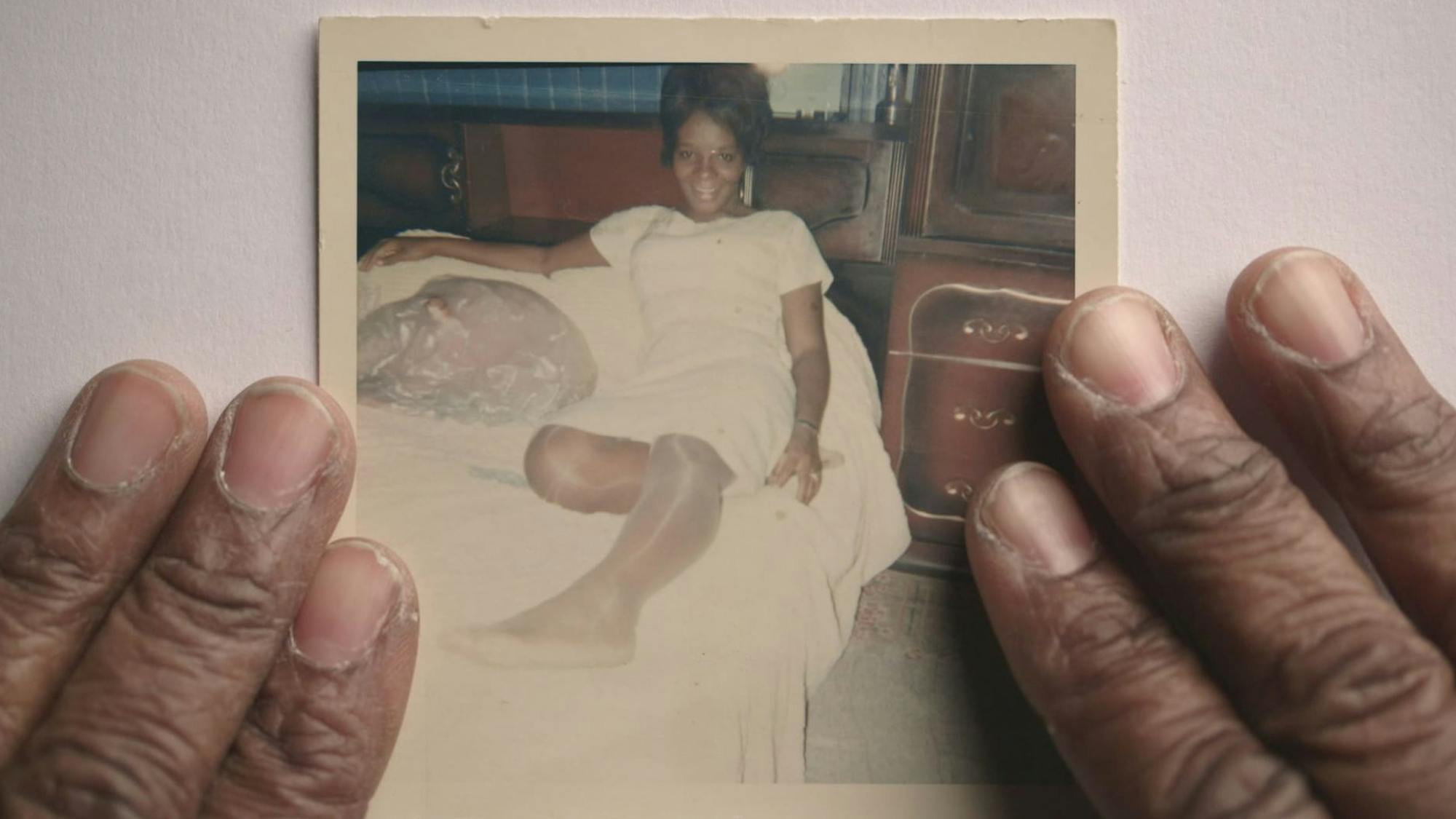 A shot from Strong Island. A pair of hands frame a polaroid of someone lounging on a bed in all white.