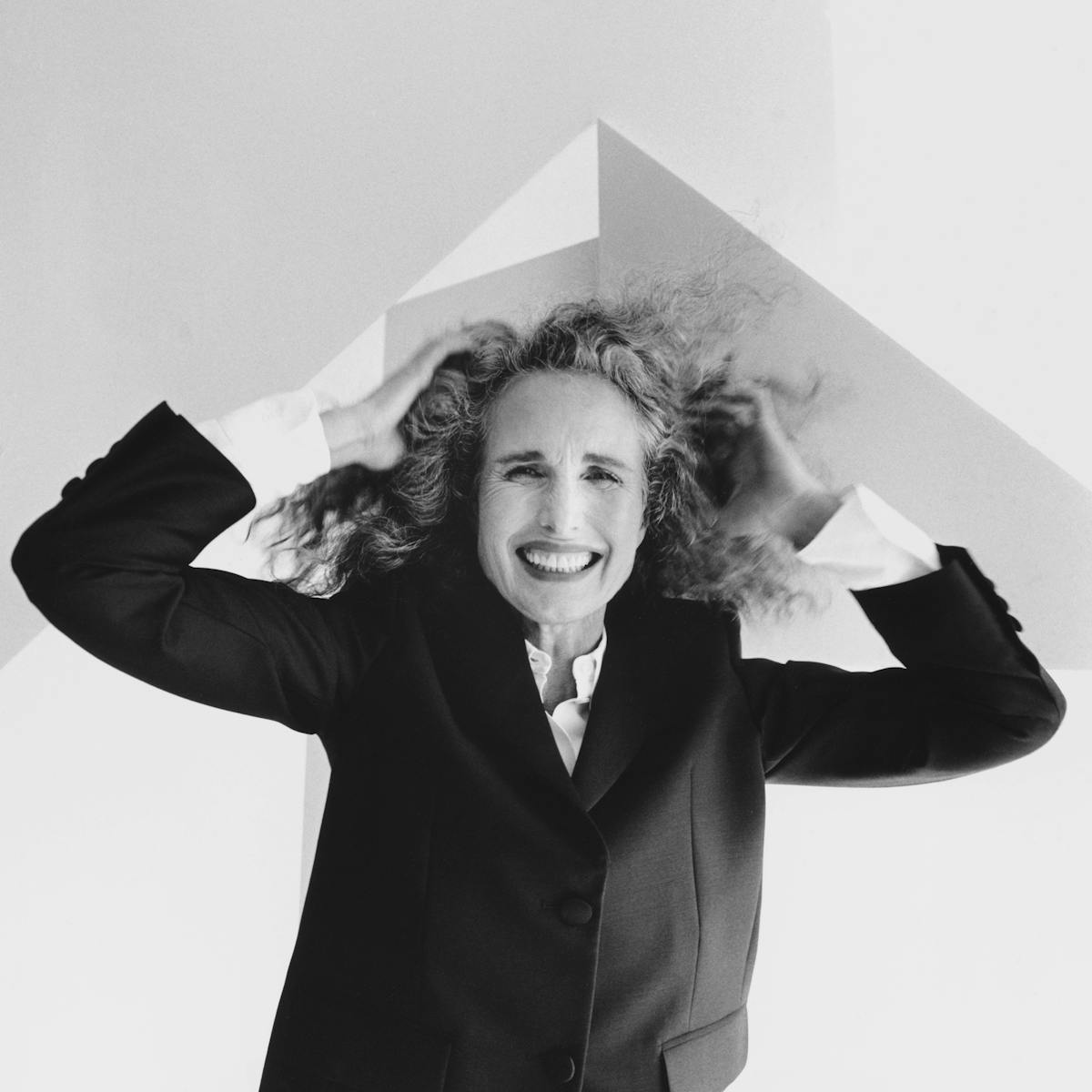 Andie MacDowell wears a black blazer and holds a sheet of paper over her head.