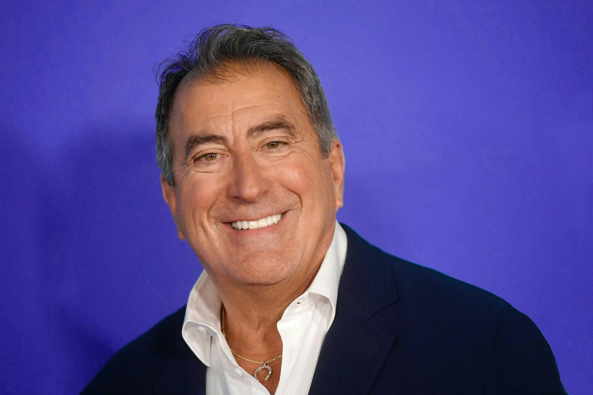 Kenny Ortega wears a navy jacket and white shirt.