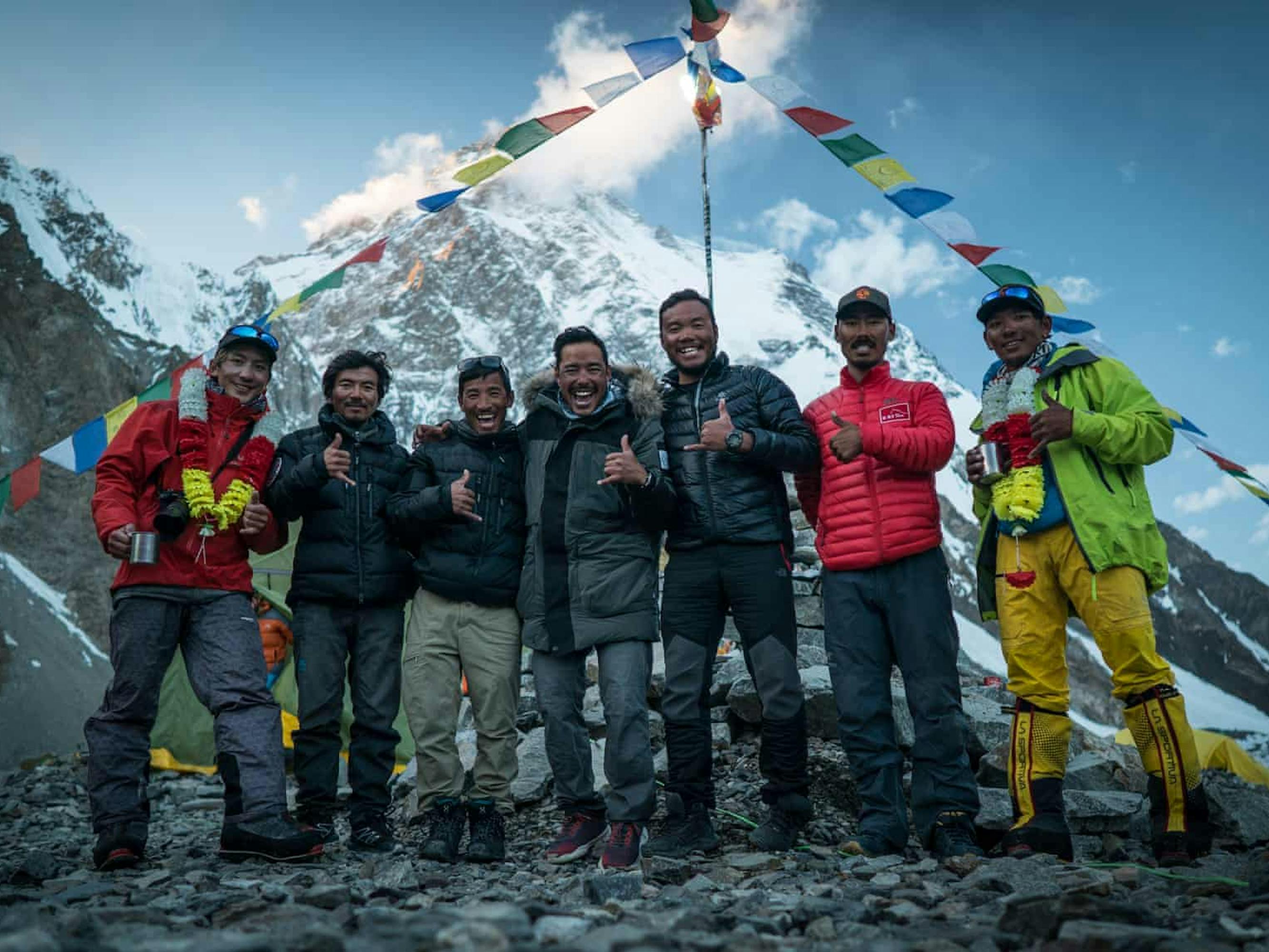 The hiking team stands at the top of a peak with flags framing their group.