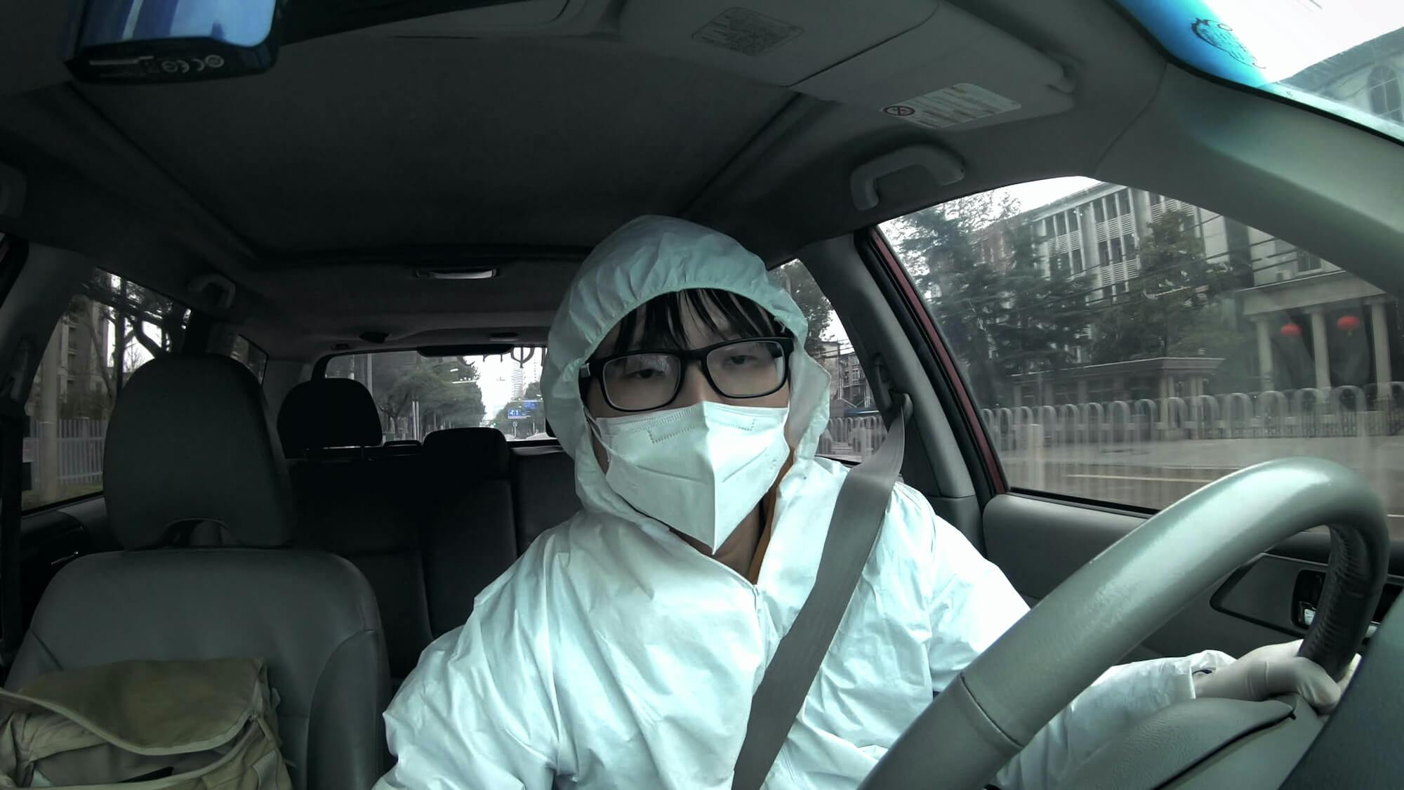 Wenhua Lin, Wuhan wears white full body protective gear as he drives a car.
