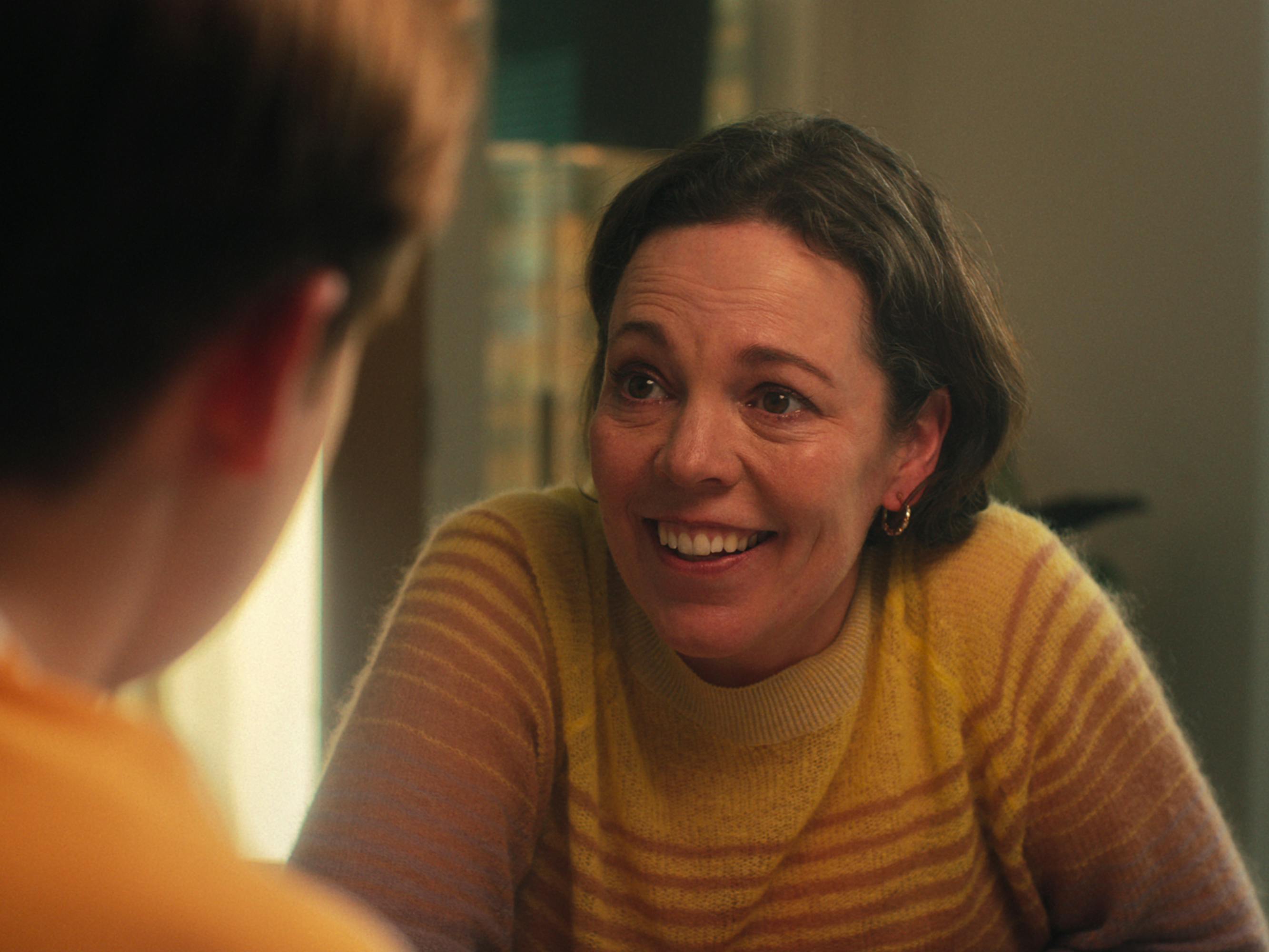 Olivia Colman Smiles in a white and brown striped sweater.