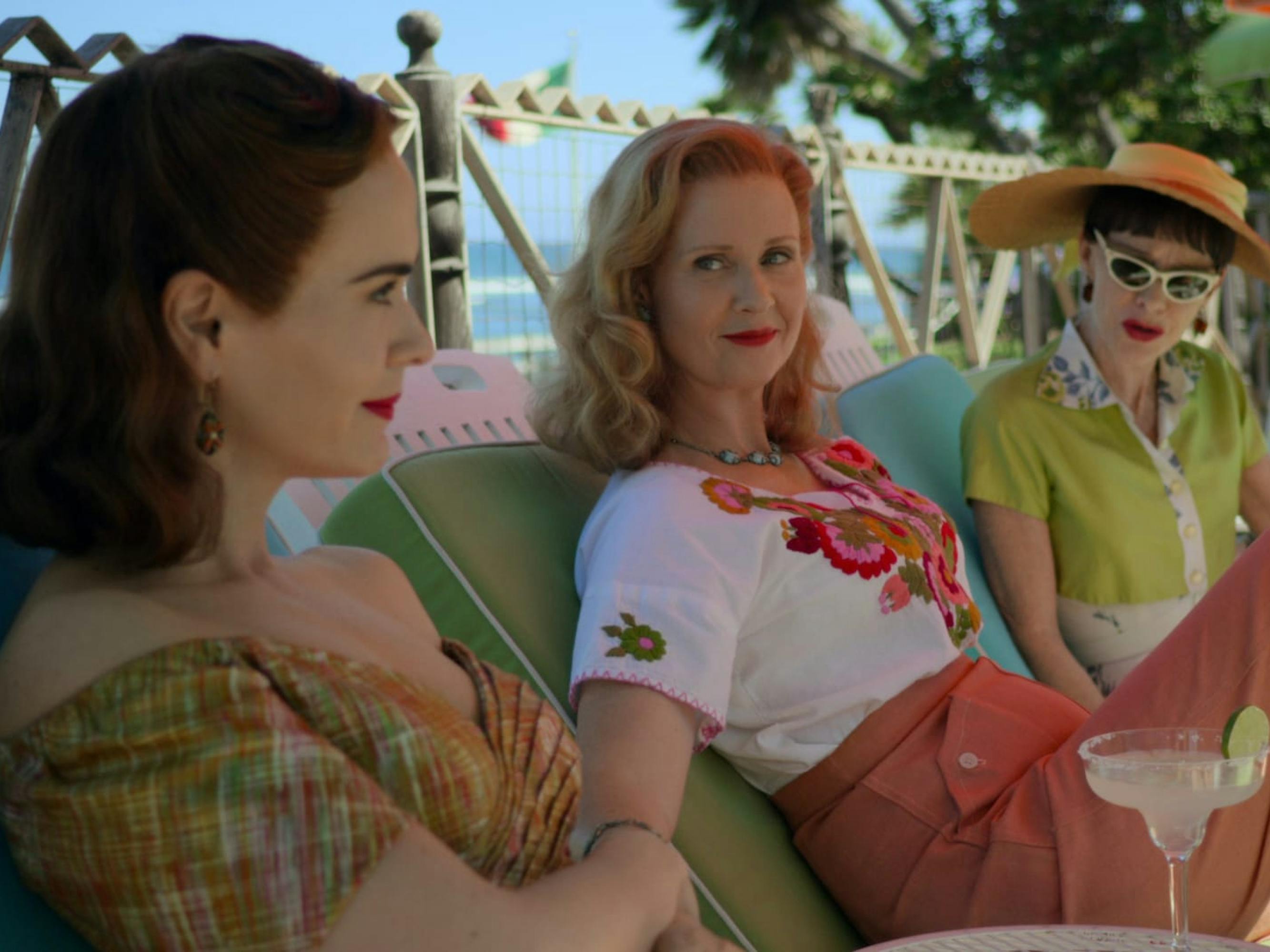 Nurse Mildred Ratched (Sarah Paulson), Gwendolyn Briggs (Cynthia Nixon), and Nurse Betsy Bucket (Judy Davis) sit outside on pool chaisses-lounges. Their hair is coiffed in classic sixties styles and they wear an assortment of bright colors, mostly pink and green. On an adjacent table sits a margarita with a lime on the side.