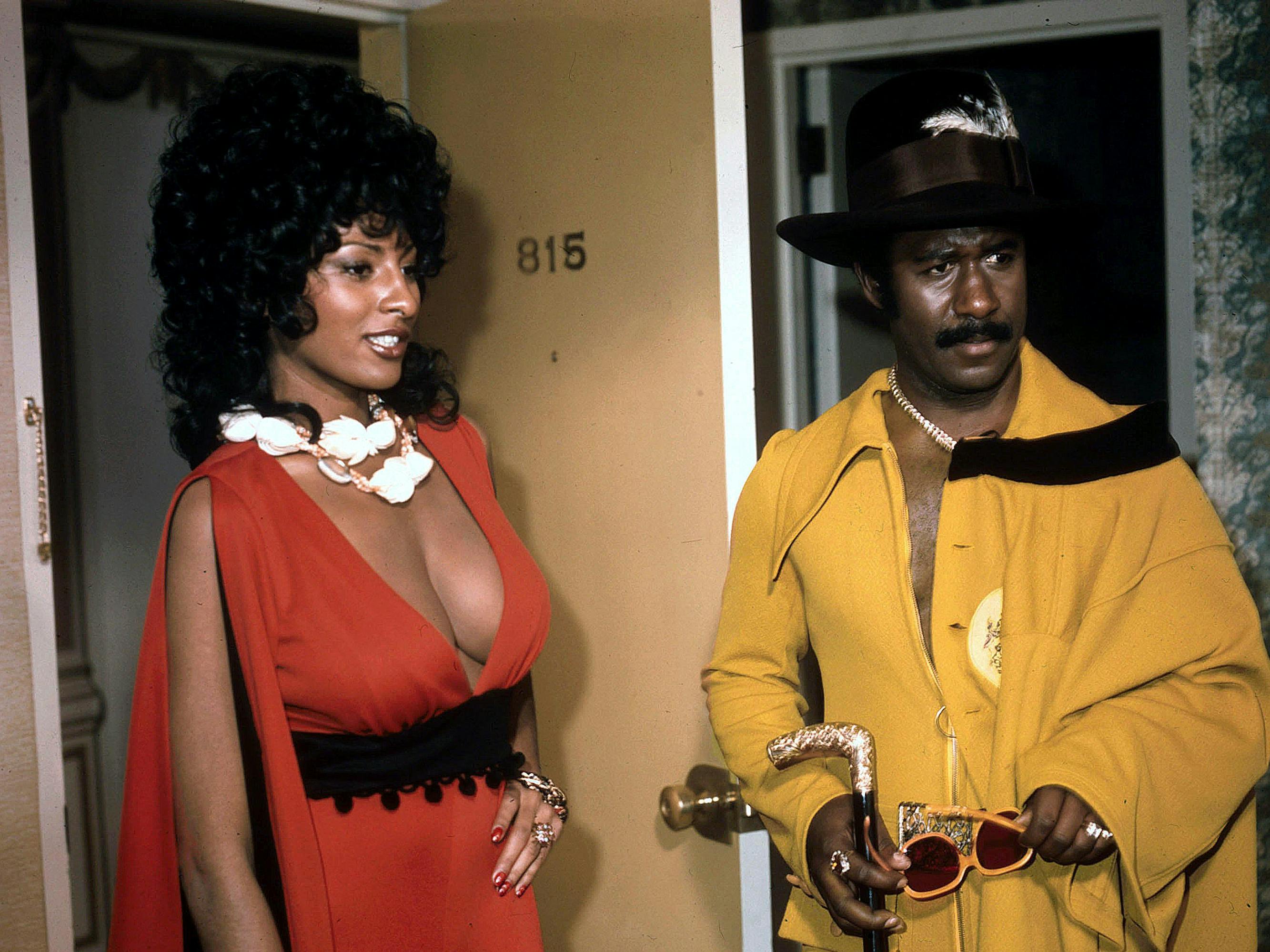 Coffy (Pam Grier) and King George (Robert DoQui) stand together in red andy yellow respectively.
