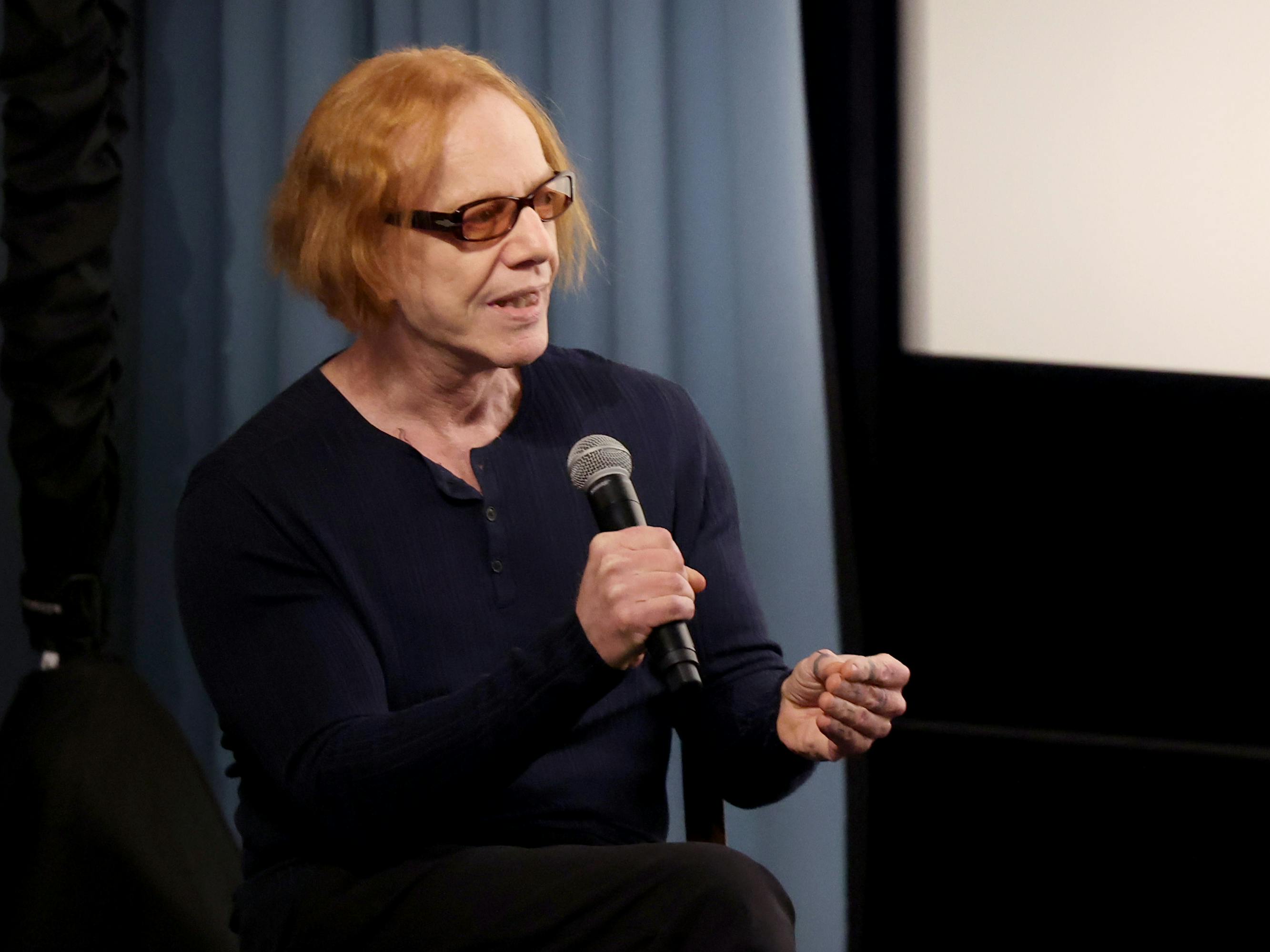 Danny Elfman wears his signature orange glasses and talks into a microphone.