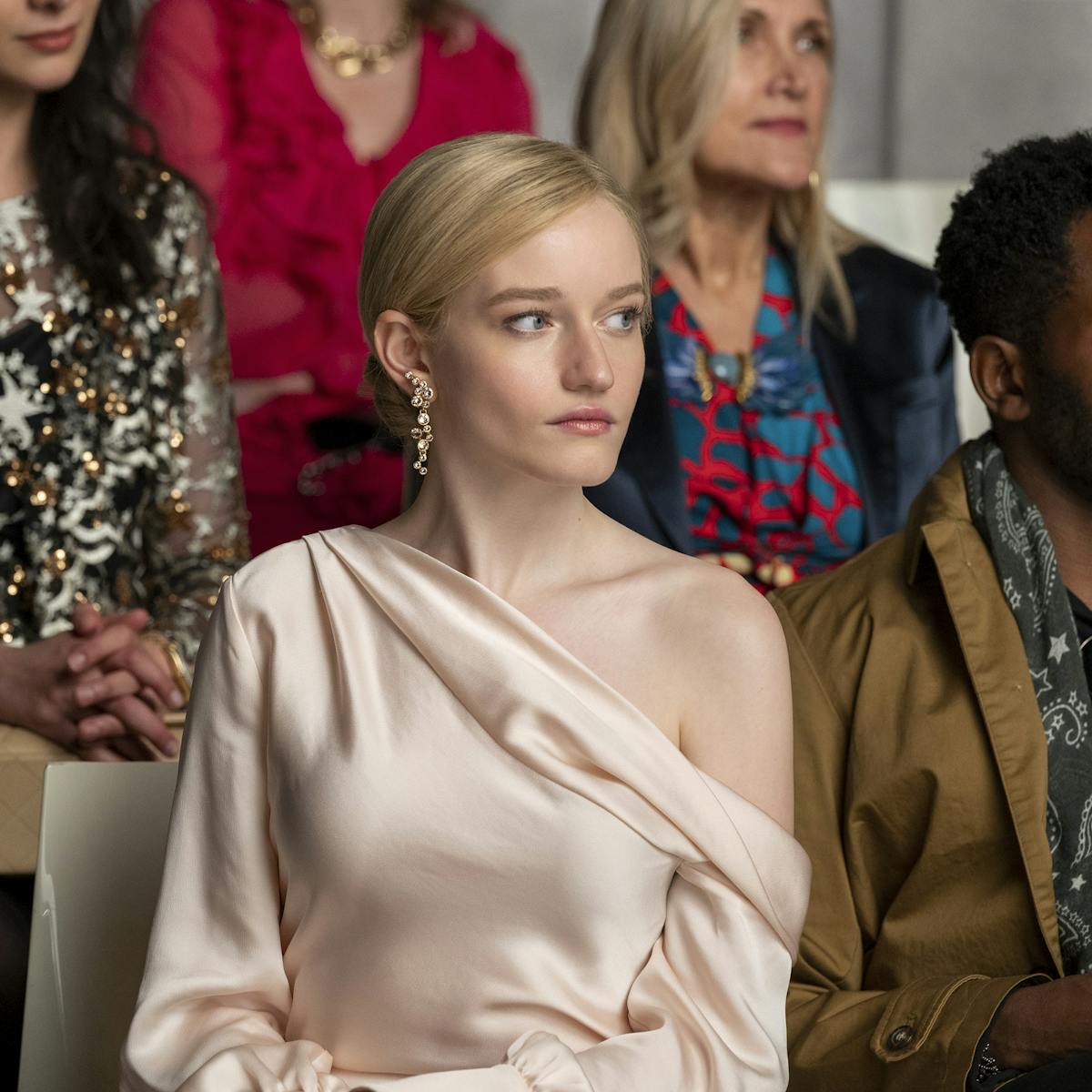 Anna Delvey wears a pale pink dress and sits front row at a fashion show.