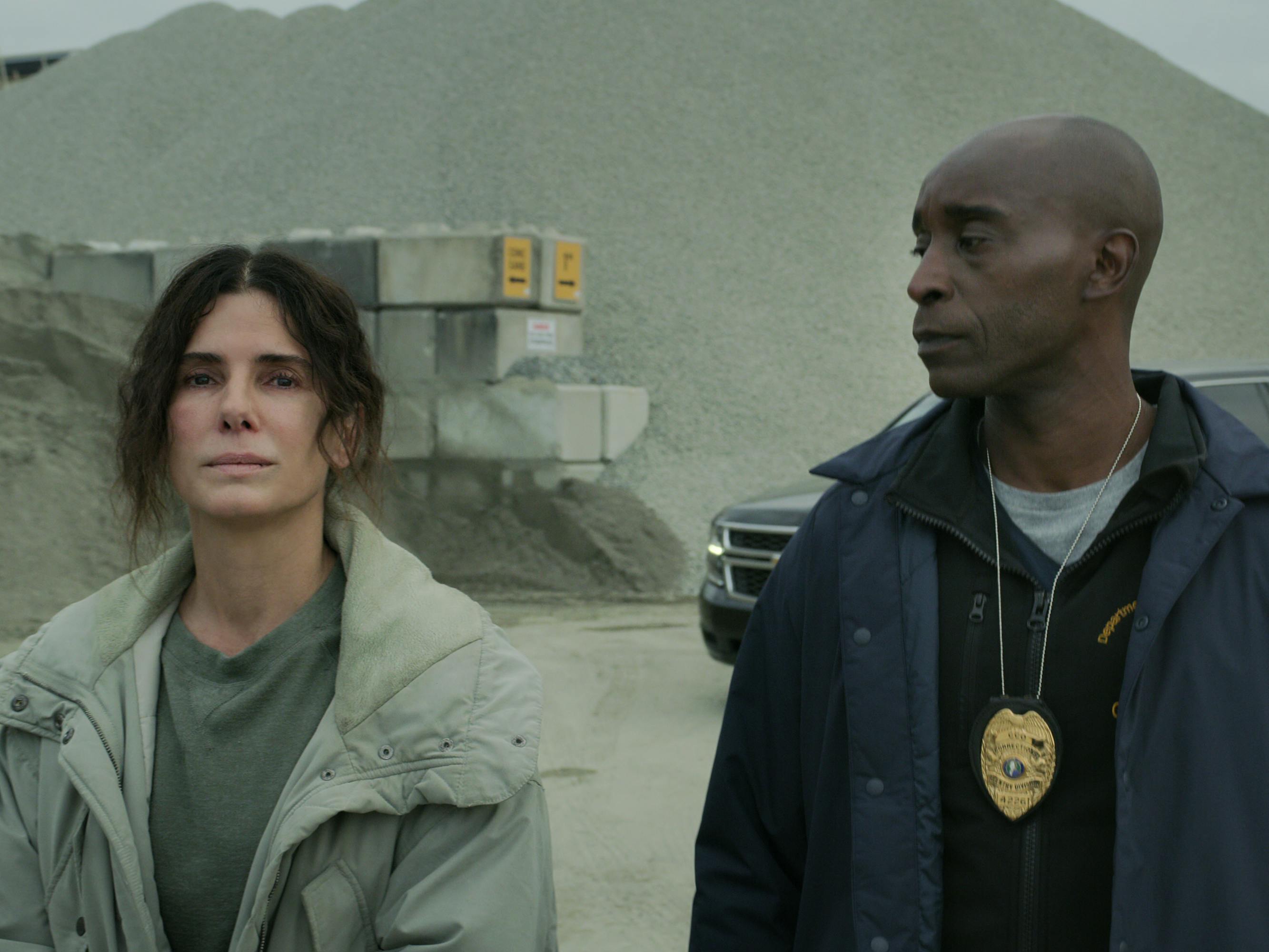 Sandra Bullock and Rob Morgan walk through a dusty lot. Bullock wears a light grey jacket, and Morgan wears a police badge over a dark jacket.
