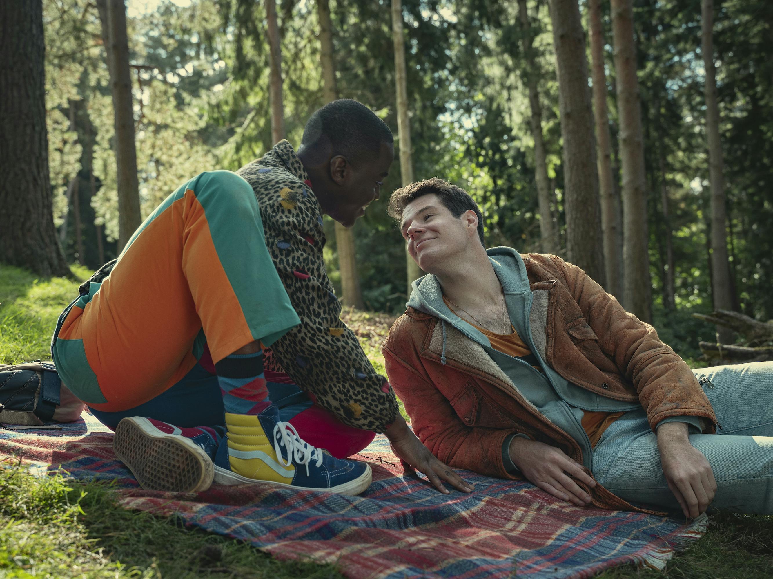 Eric Effiong (Ncuti Gatwa) and Adam Groff (Connor Swindells) look romantic on a picnic blanket. 