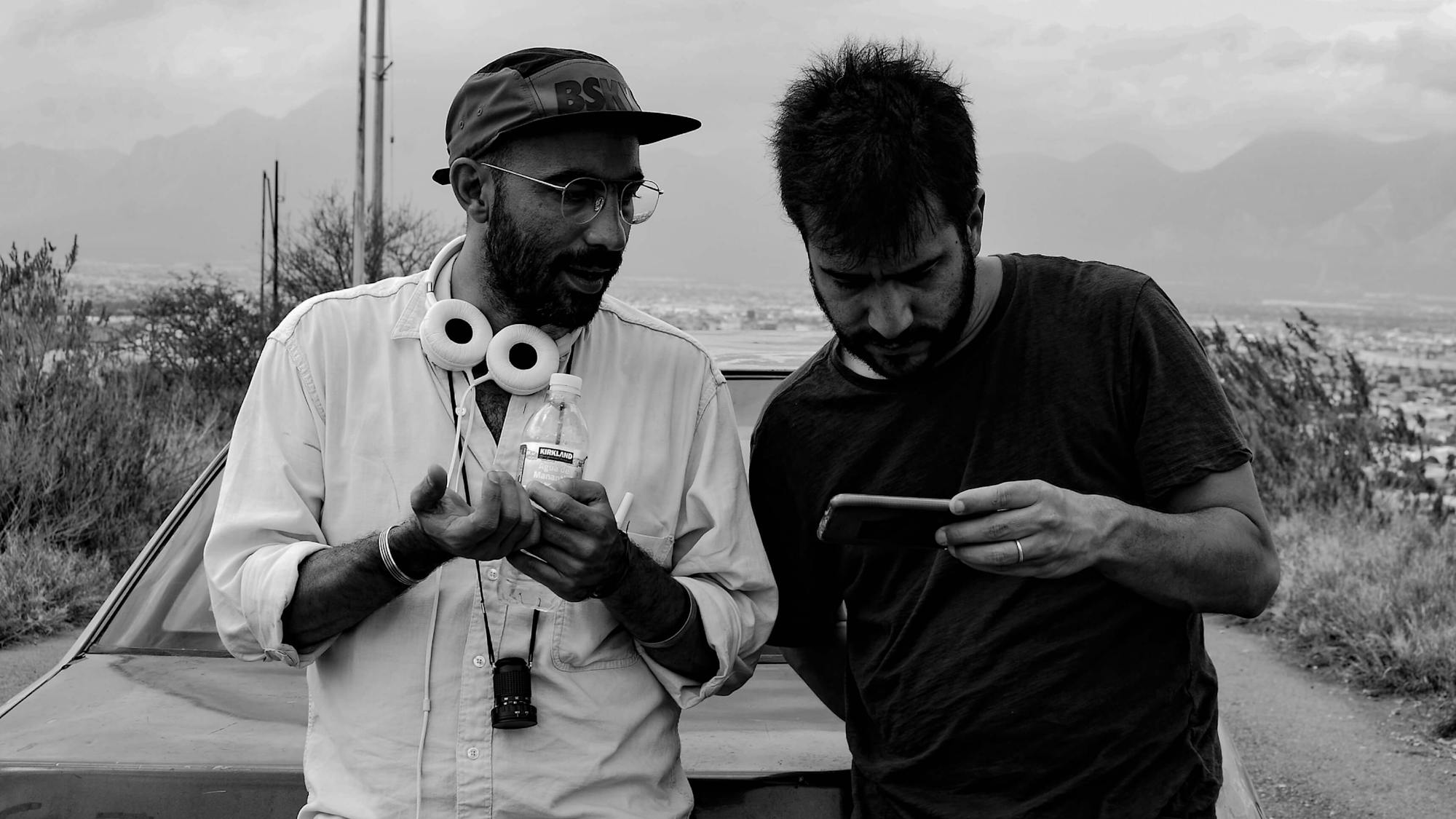 Fernando Frías de la Parra and TK lean against an old car in the hills of Monerrey in this black-and-white photograph.