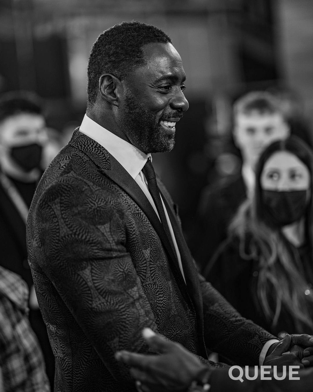 Idris Elba in a patterned tuxedo jacket shakes hands on the red carpet