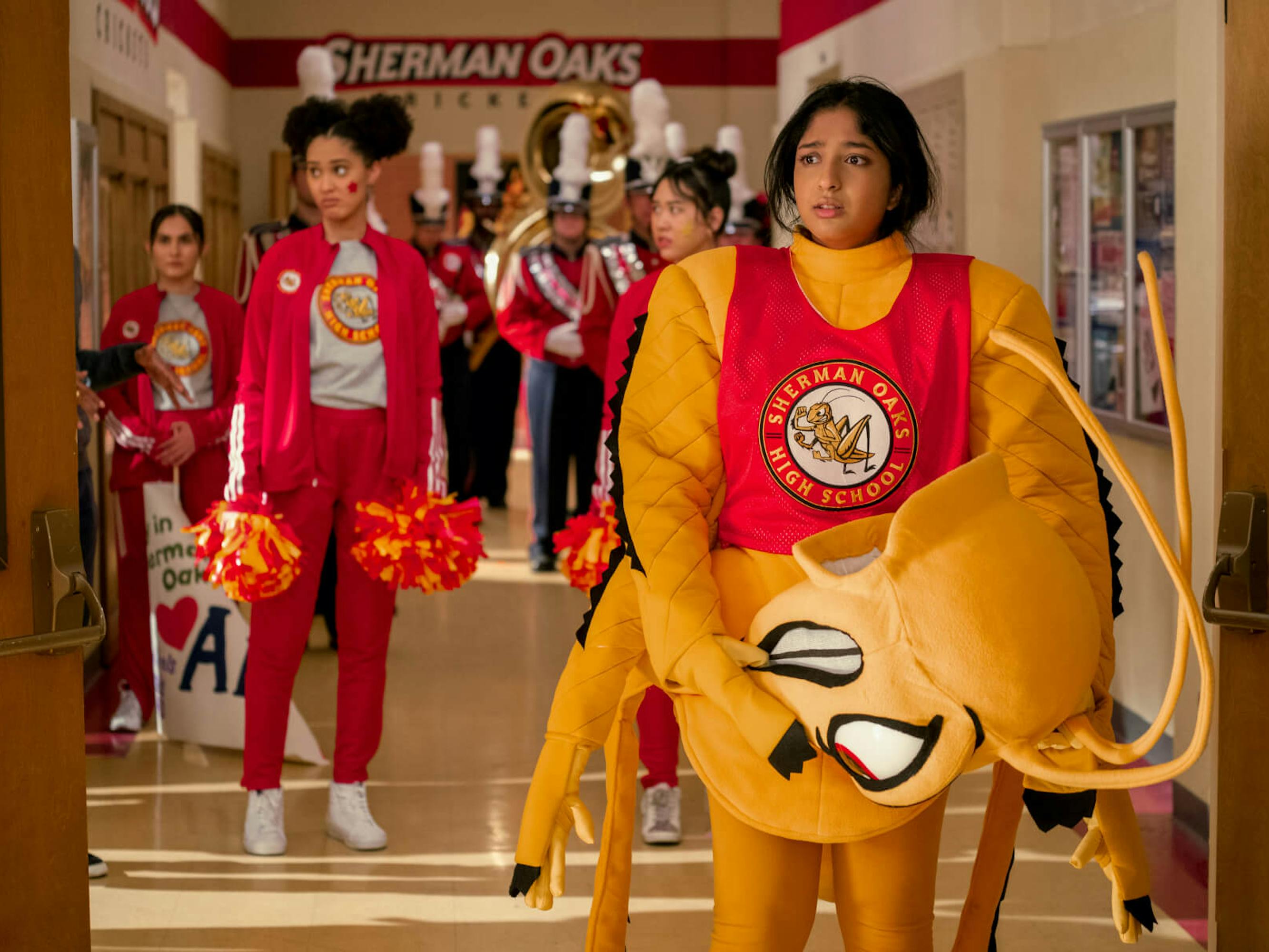 Fabiola Torres (Lee Rodriguez), Eleanor Wong (Ramona Young), and Devi Vishwakumar (Maitreyi Ramakrishnan) wear outfits exhibiting their school spirit: from red track suits to a full-on cricket costume.