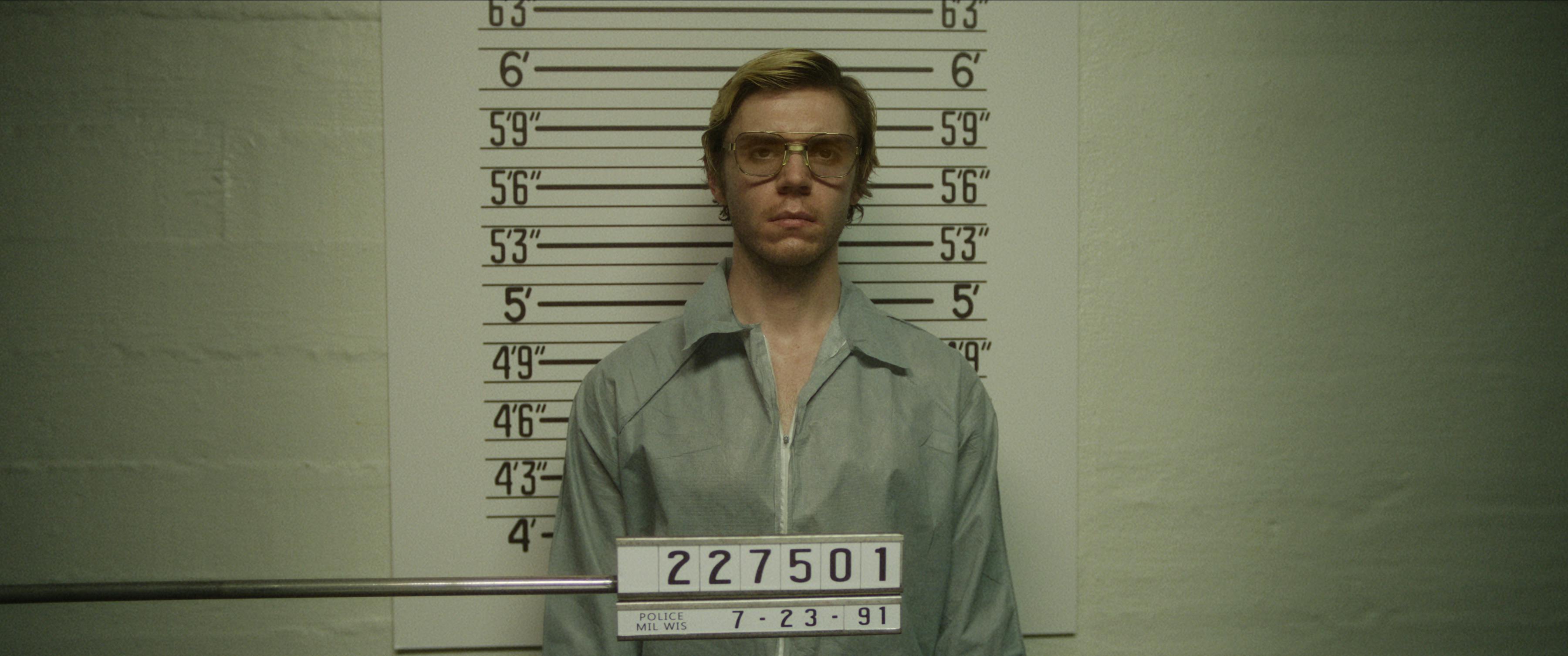 Jeffrey Dahmer (Evan Peters) stands in front of a wall getting his mugshot taken.