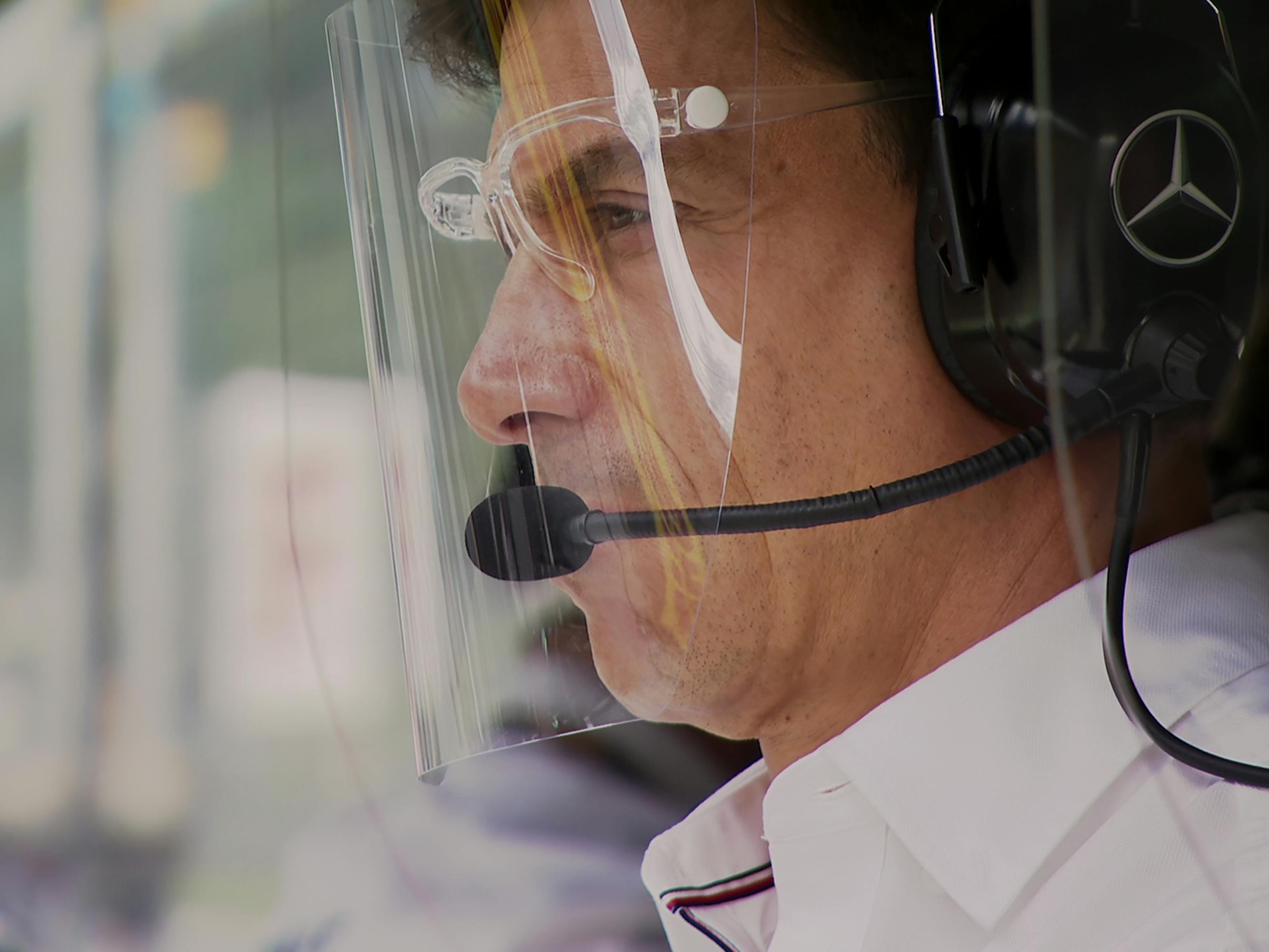 Toto Wolff wears a plastic PPE mask over his face and a headset with a microphone. 