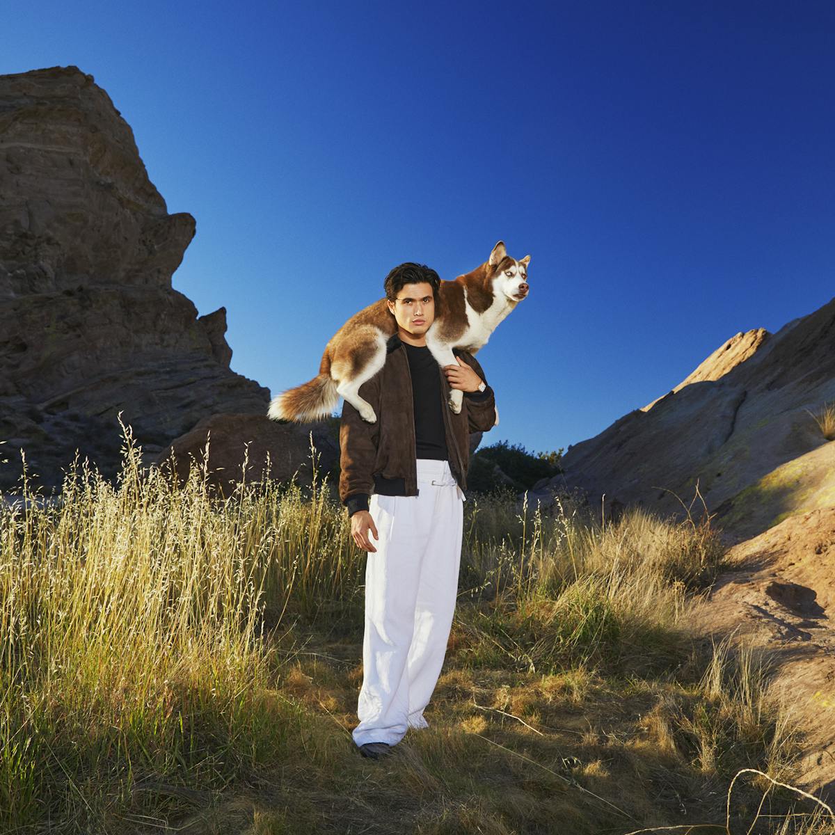 Charles Melton stands in the desert with his dog, Neya, wrapped around his shoulders.