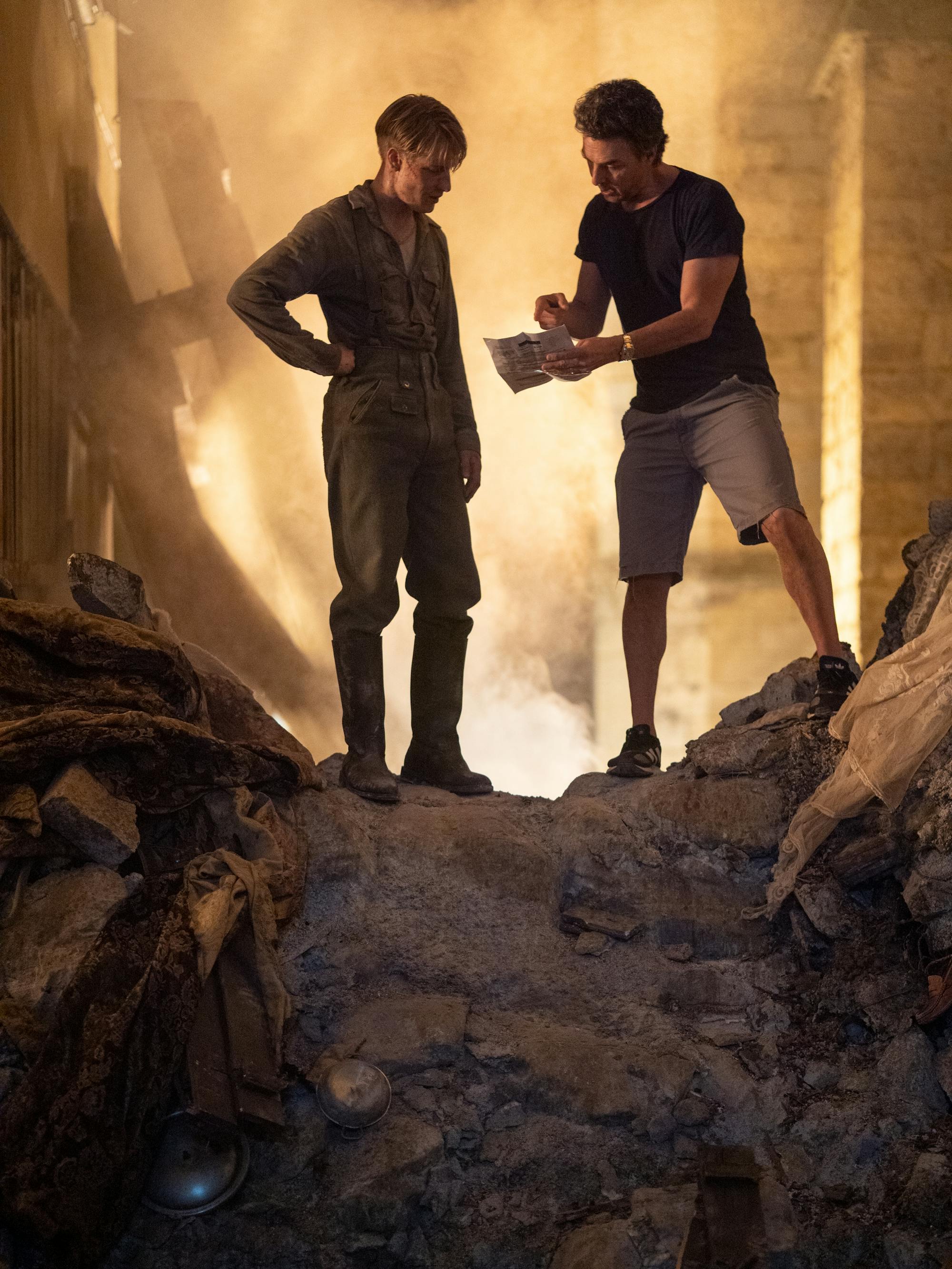 Louis Hofmann and Shawn Levy behind the scenes on set. The two stand over a dusty, dark, rocky slide.