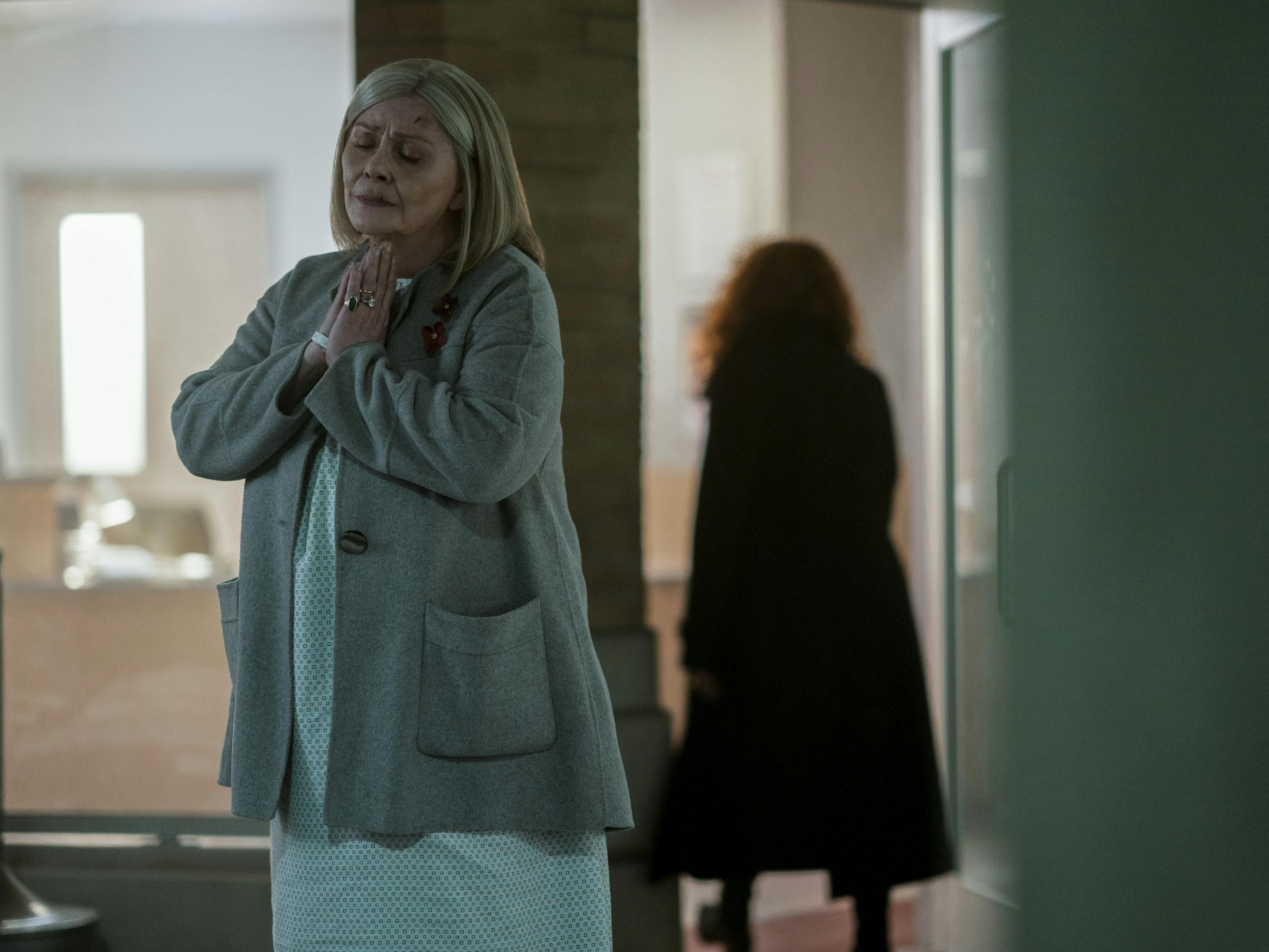 Ruth Brenner (Elizabeth Ashley) and Nadia Vulvokov (Natasha Lyonne) stand outside. Ruth wears a hospital gown and a grey cardigan. Nadia has her back to the camera.