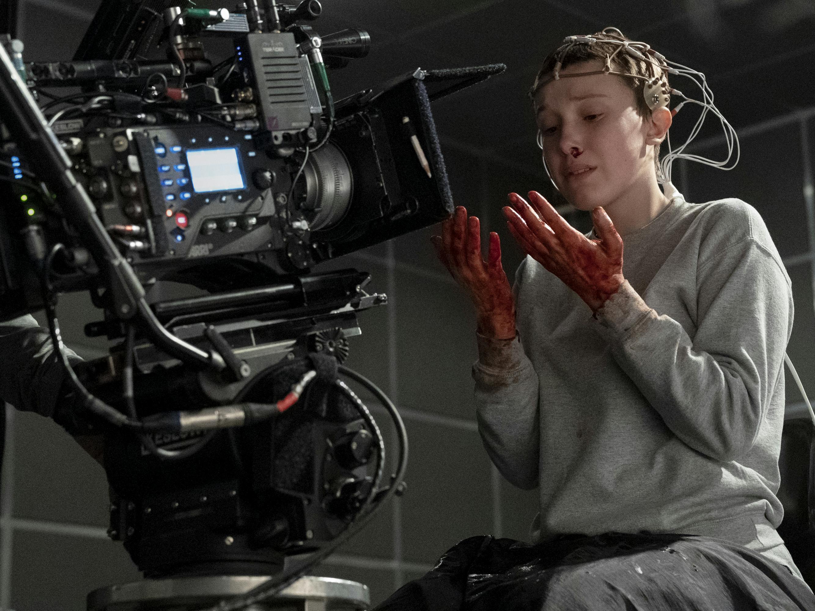 Eleven (Millie Bobby Brown) looks alarmingly at her bloody hands, while a camera rig looms near.
