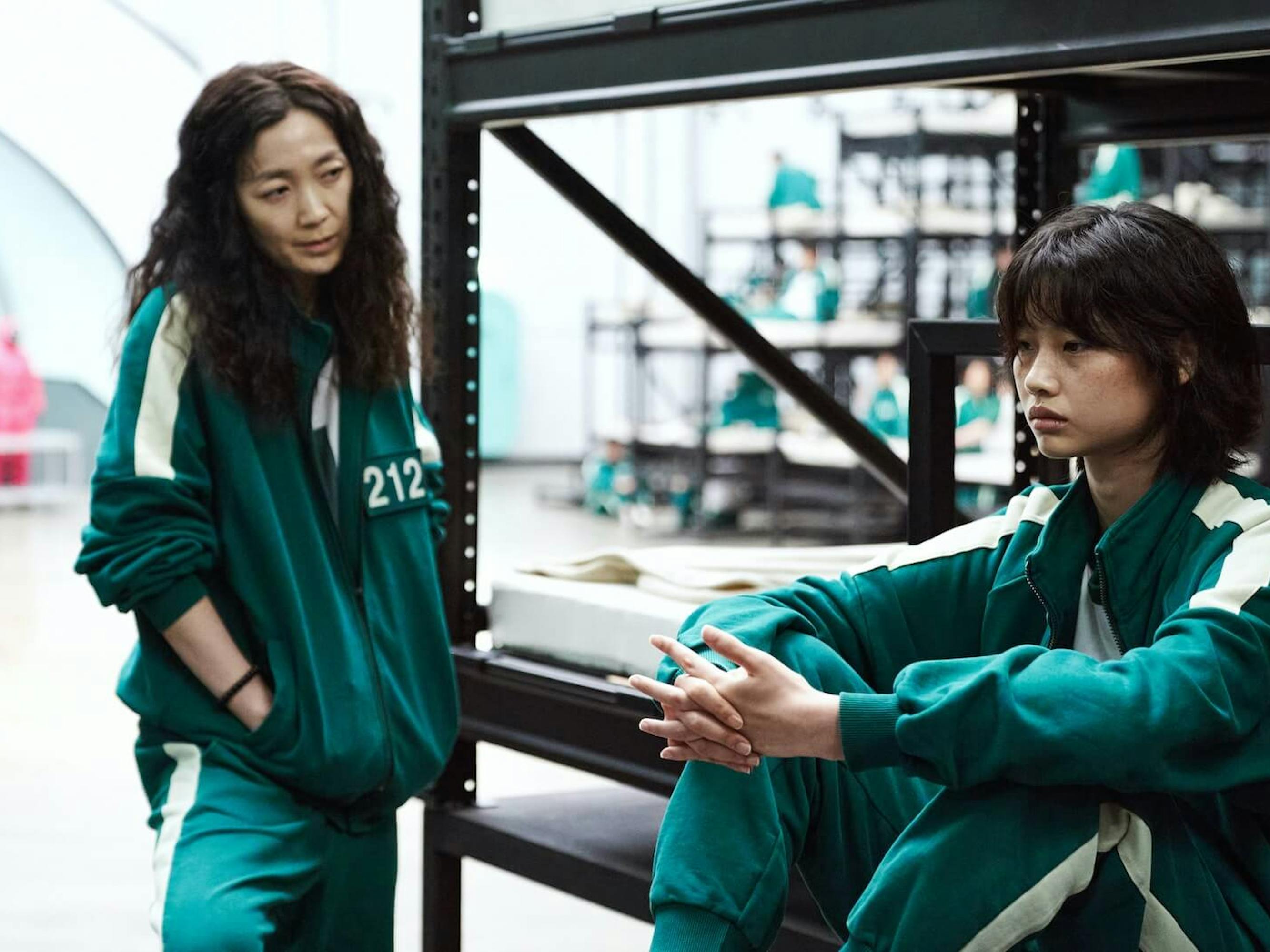 Mi-nyeo (Kim Joo-ryoung) and Sae-byeok (Jung Ho-yeon) stand in an industrial looking warehouse in their green tracksuits.