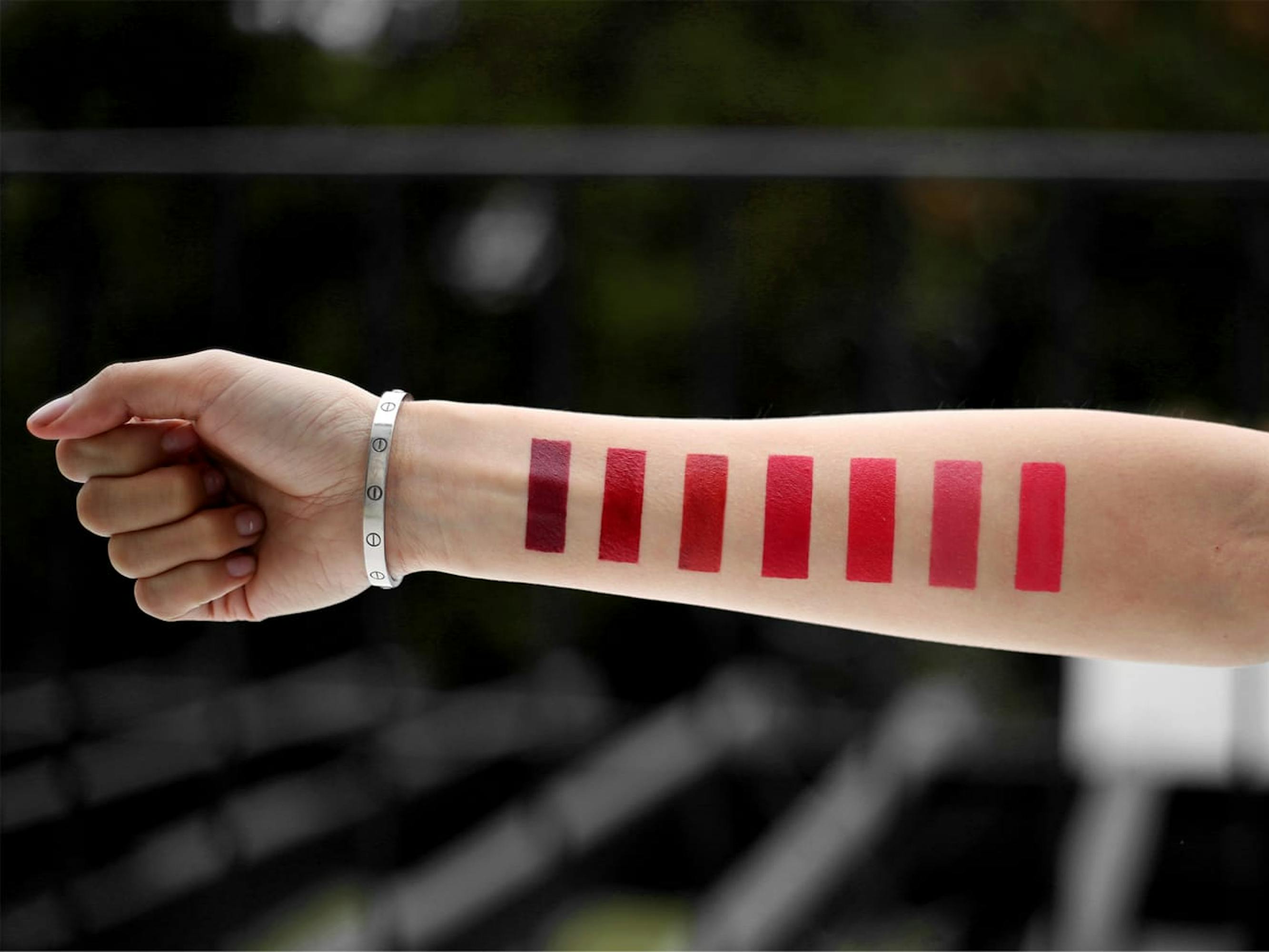 A makeup artist holds out her arm, on which perfectly rectangular lipstick swatches have been drawn. 