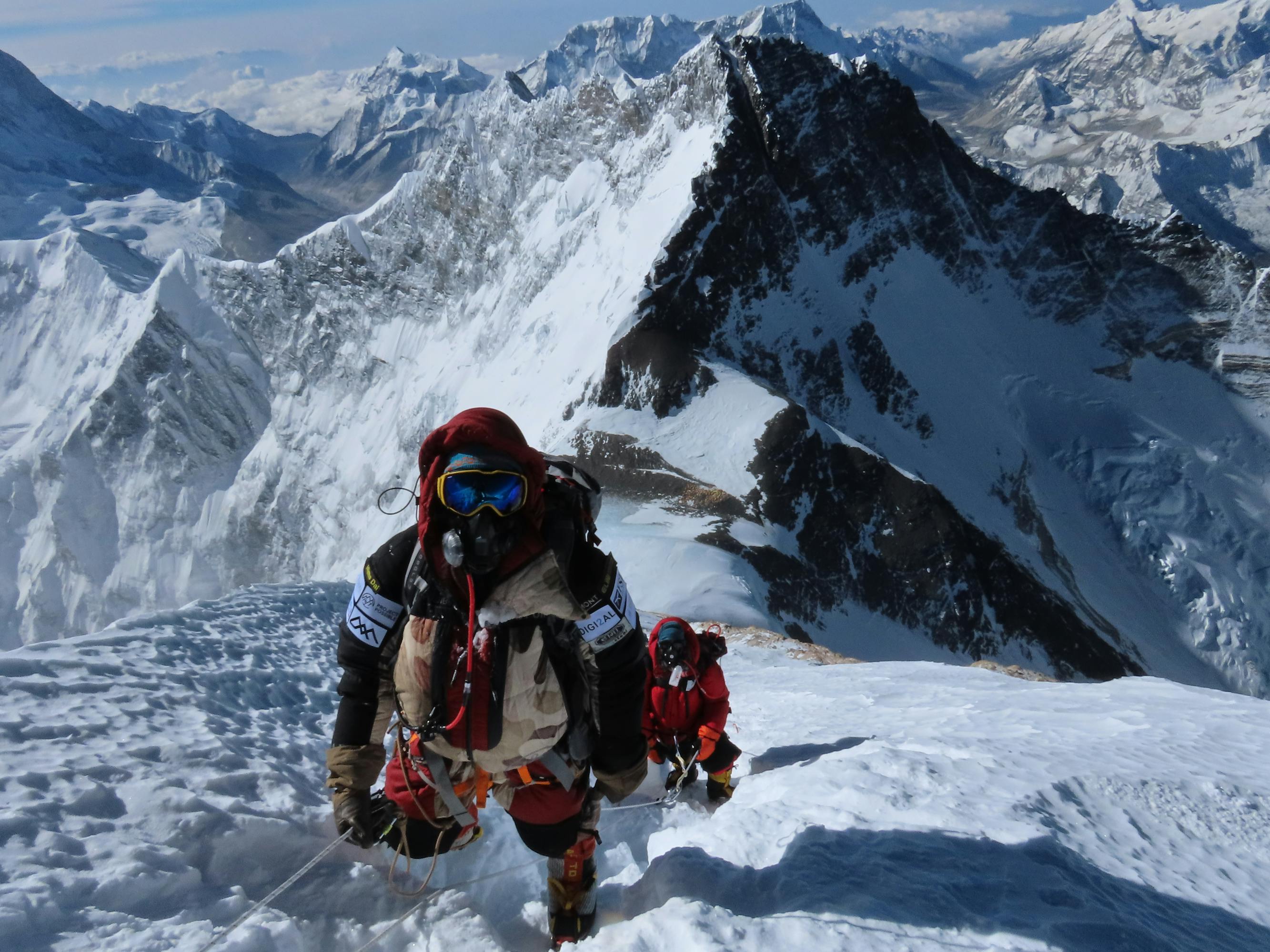 Hikers straddle a rope up a snowy ledge.