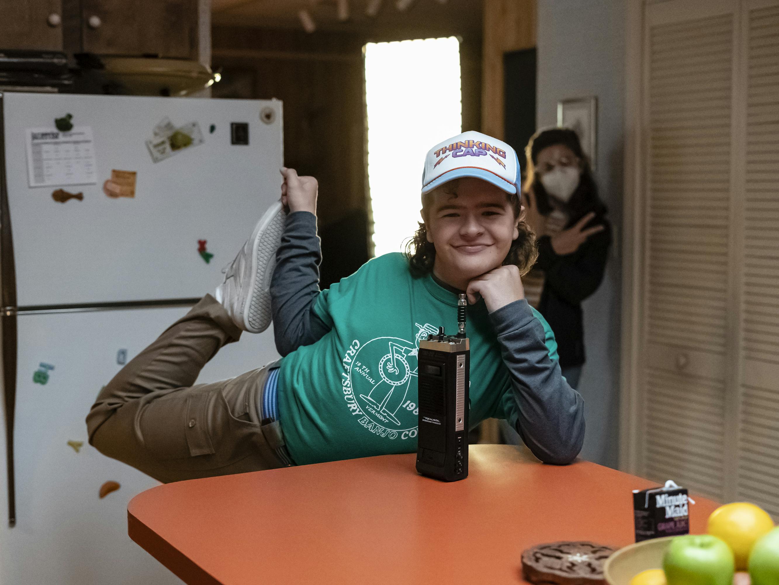 Dustin Henderson (Gaten Matarazzo) does the dancer yoga position and smiles, as he rests his chin in his palm.