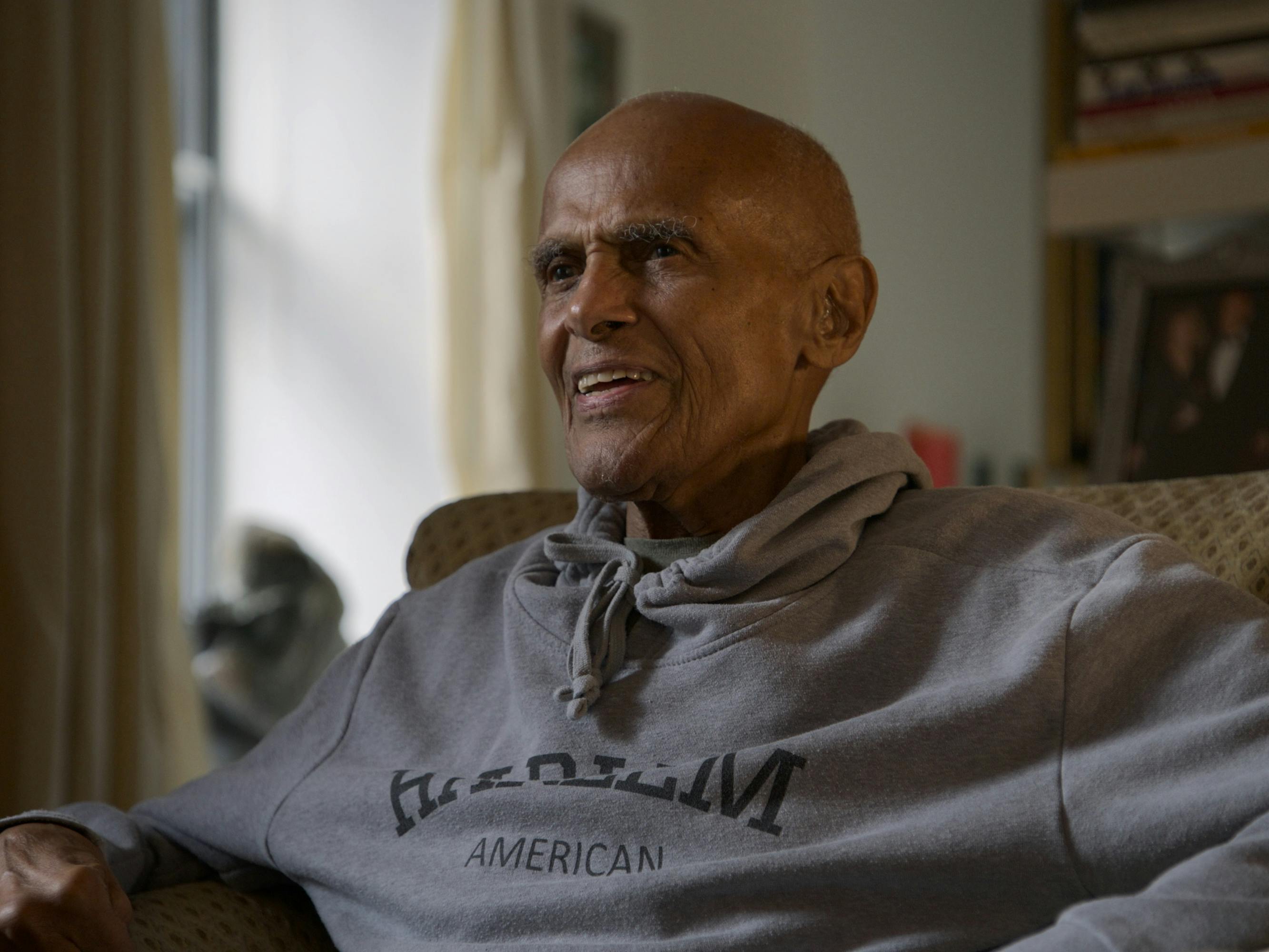 Harry Belafonte wears a sweatshirt and sits in a comfy armchair.