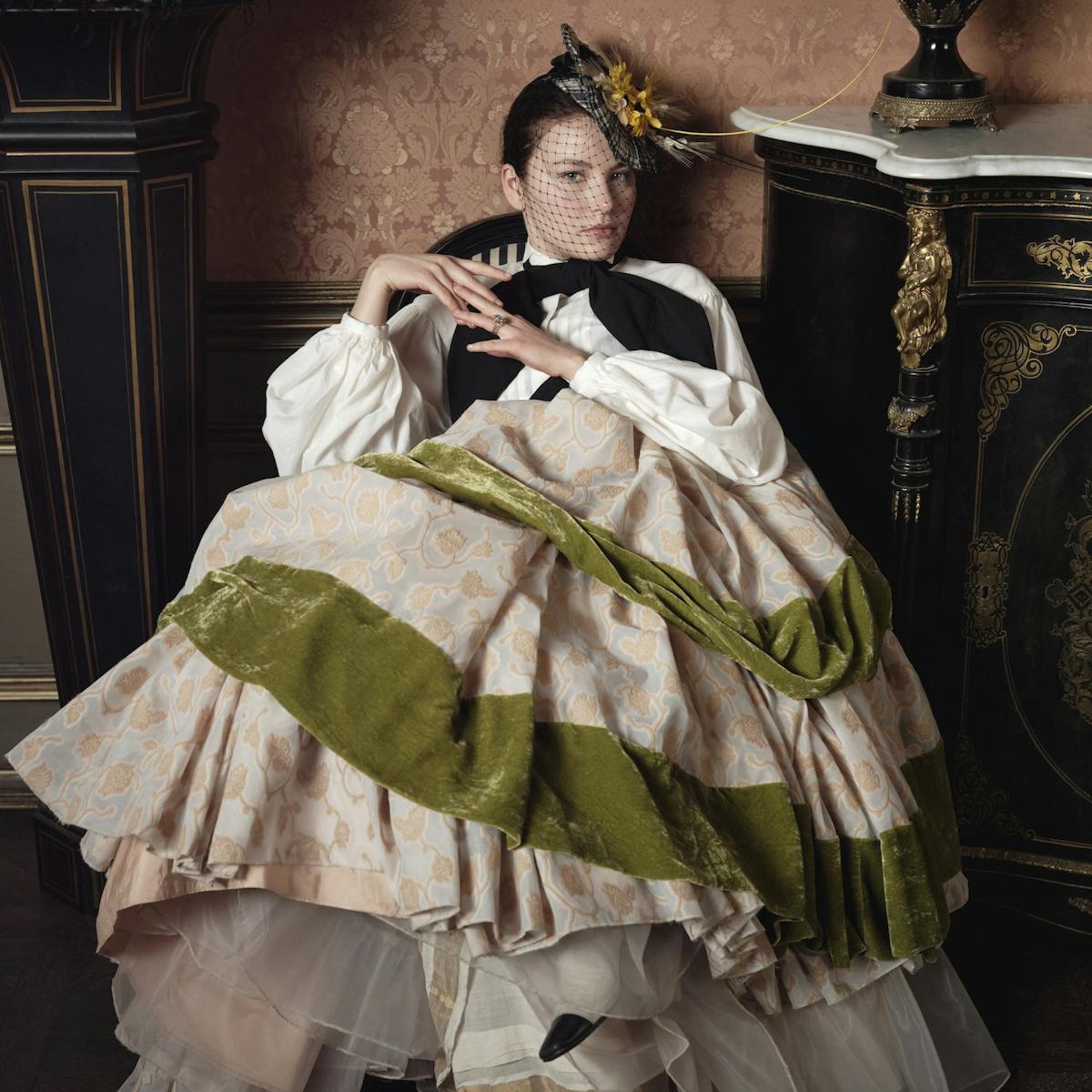 The empress wears a white and green dress with a black bow.