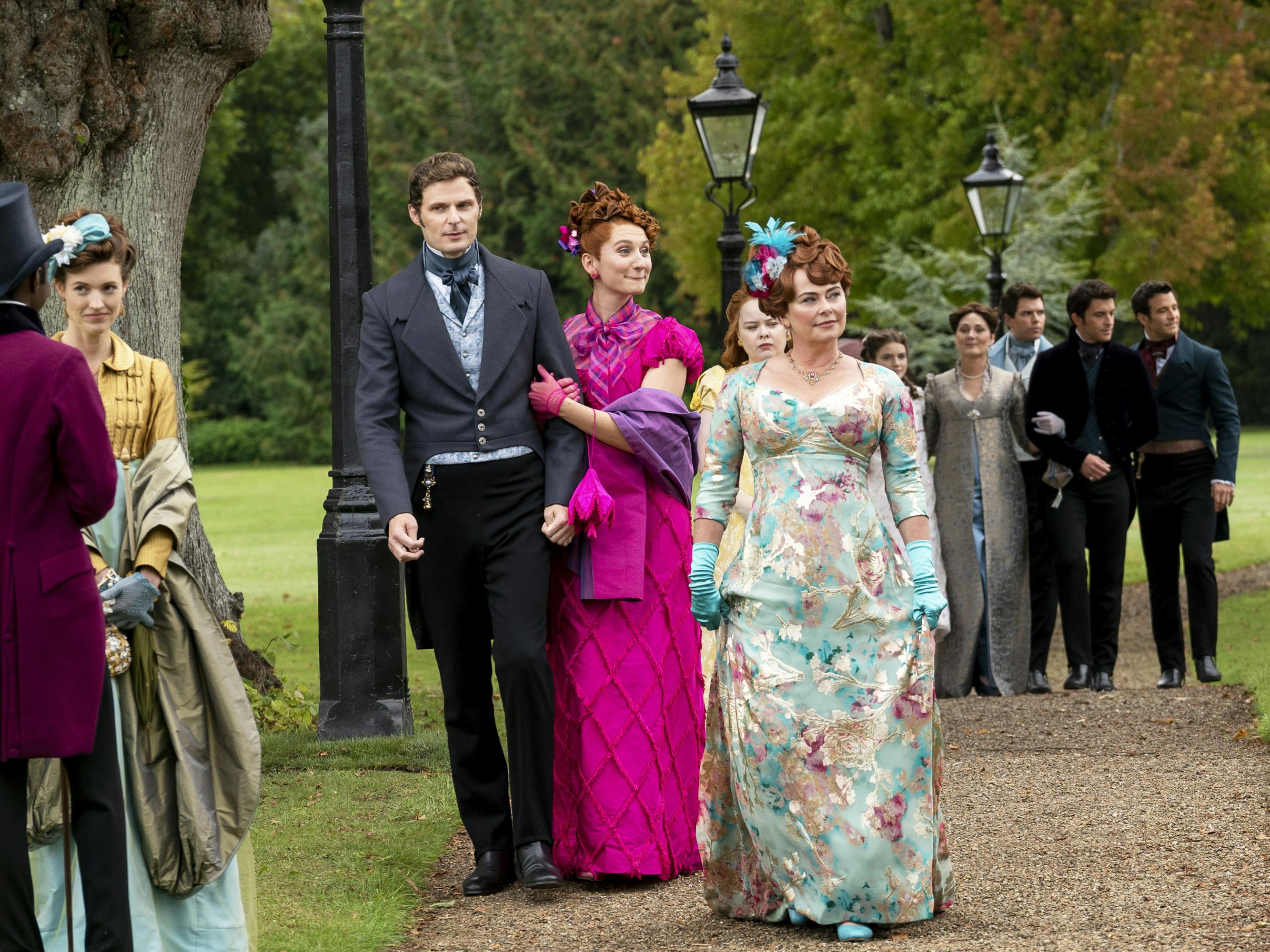 Lord Jack Featherington (Rupert Young), Prudence Featherington (Bessie Carter), Penelope Featherington (Nicola Coughlan), Lady Portia Featherington (Polly Walker), Hyacinth Bridgerton (Florence Emilia Hunt), Lady Violet Bridgerton (Ruth Gemmell), Colin Bridgerton (Luke Newton), Anthony Bridgerton (Jonathan Bailey), and Benedict Bridgerton (Luke Thompson) walk through the park in clusters. The tension is high, even in this still!