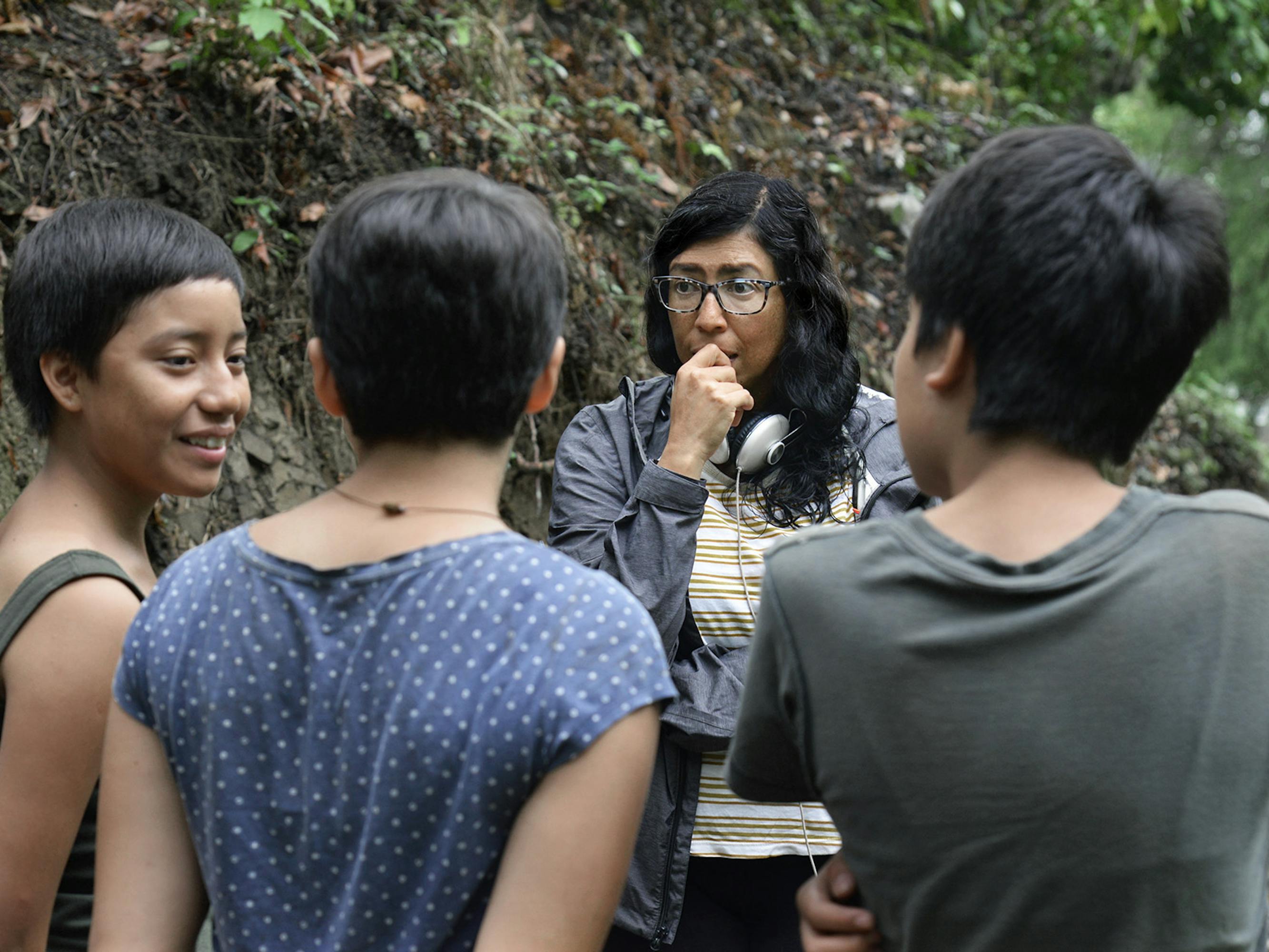 Three girls huddle around Tatiana Huezo outside. They have short hair, and wear green and blue shirts.