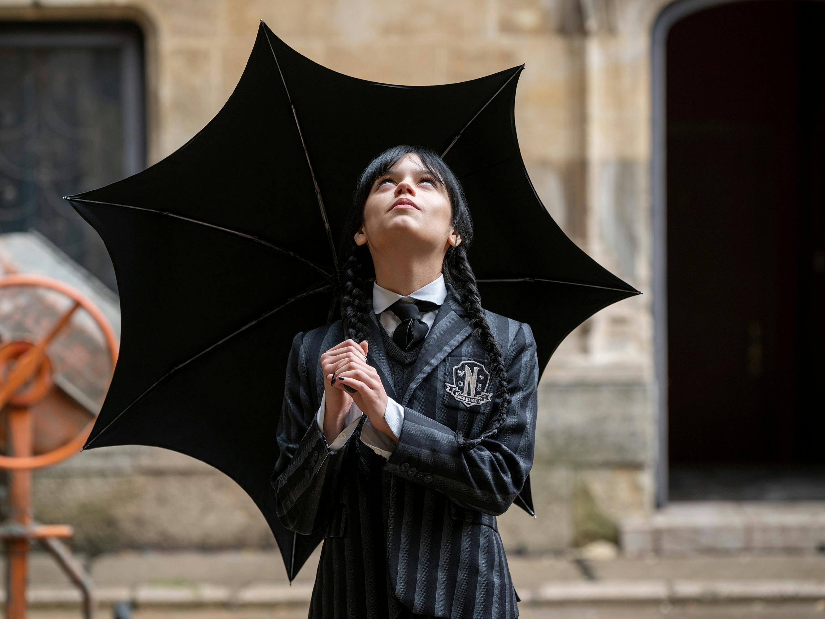 Wednesday (Jenna Ortega) wears all black and holds an umbrella.