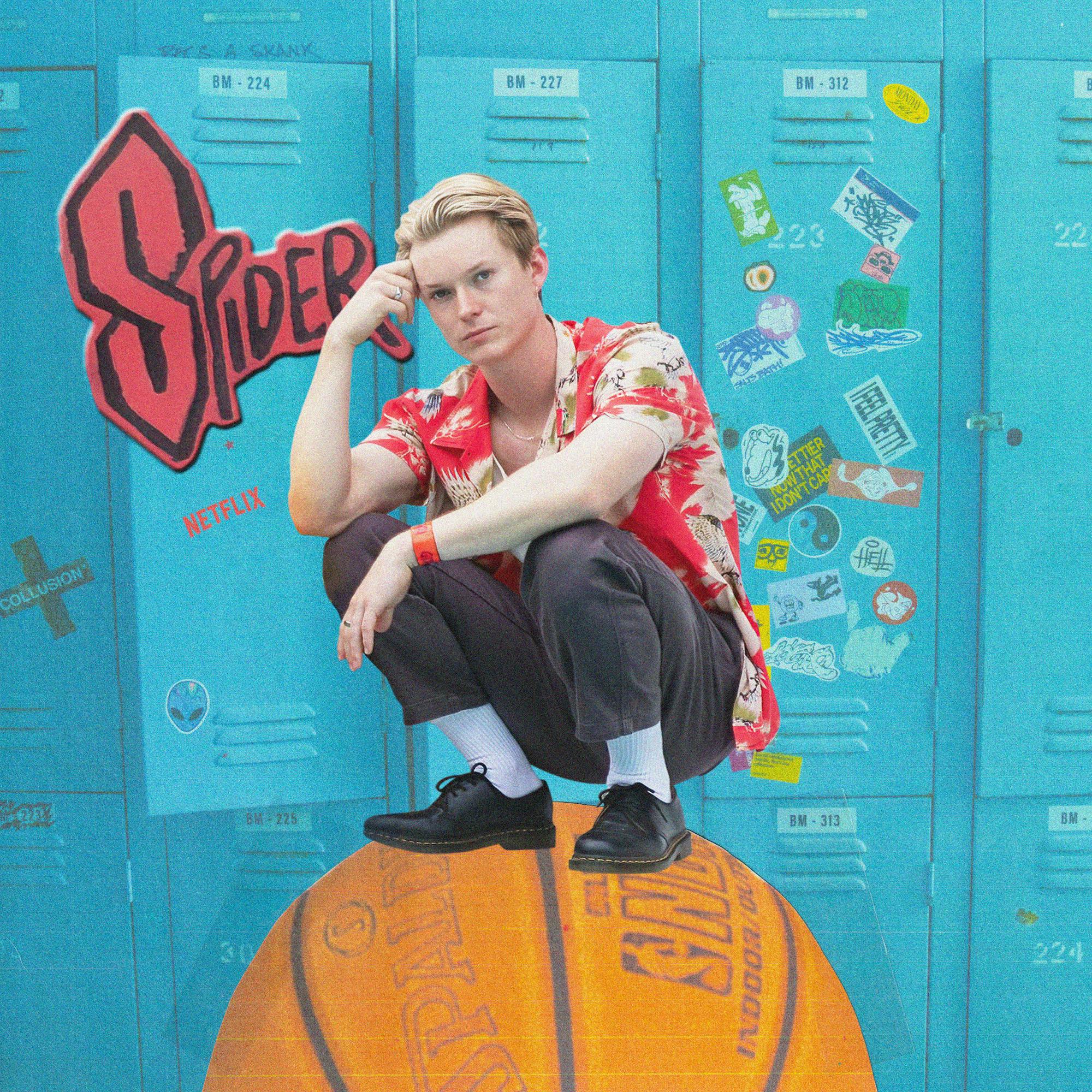 Bryn Chapman Parish plays Spider. He stands on a basketball in front of some blue lockers.