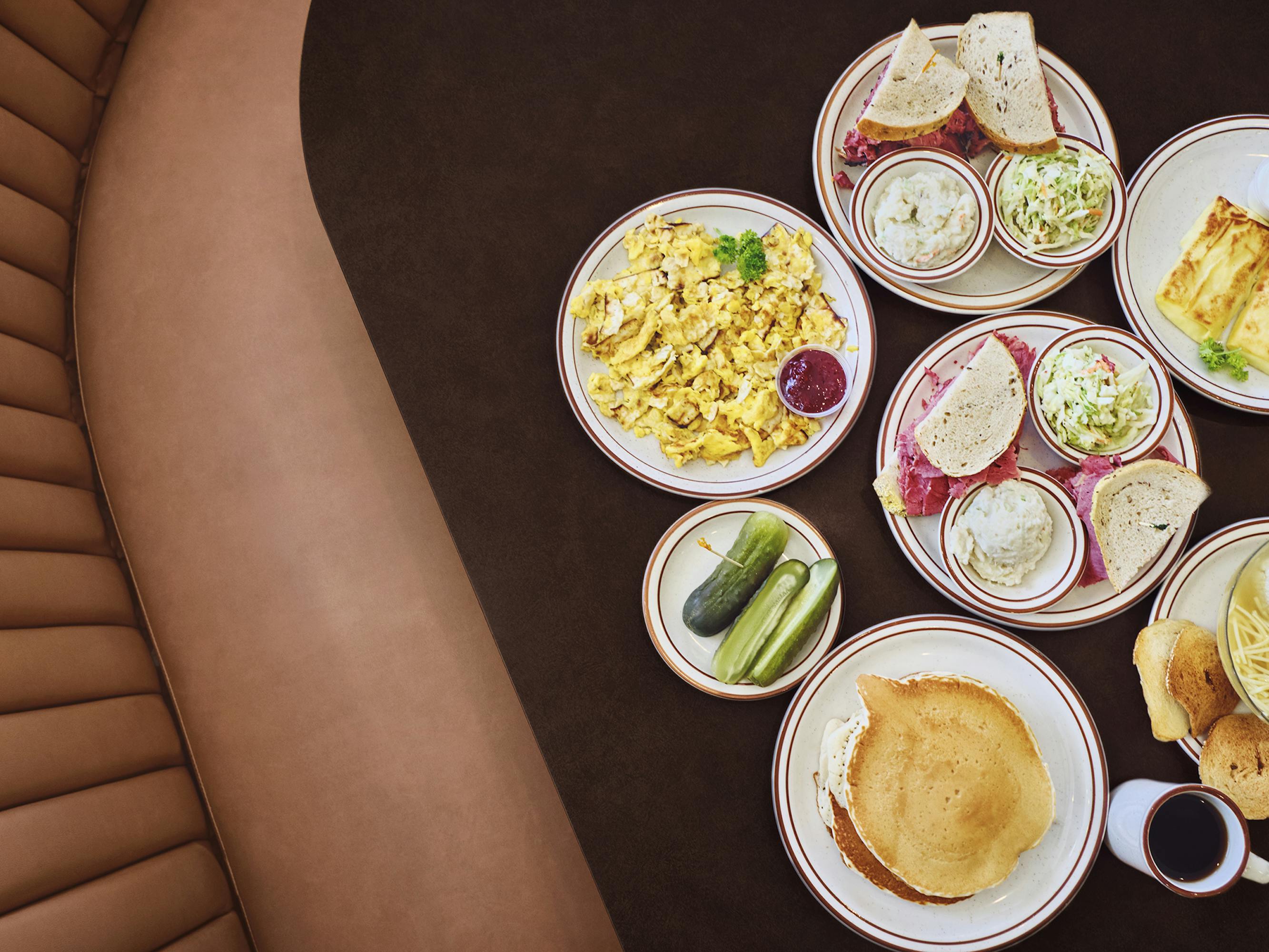 An array of deli foods: pickles, pancakes, sandwiches, eggs, and sauces.