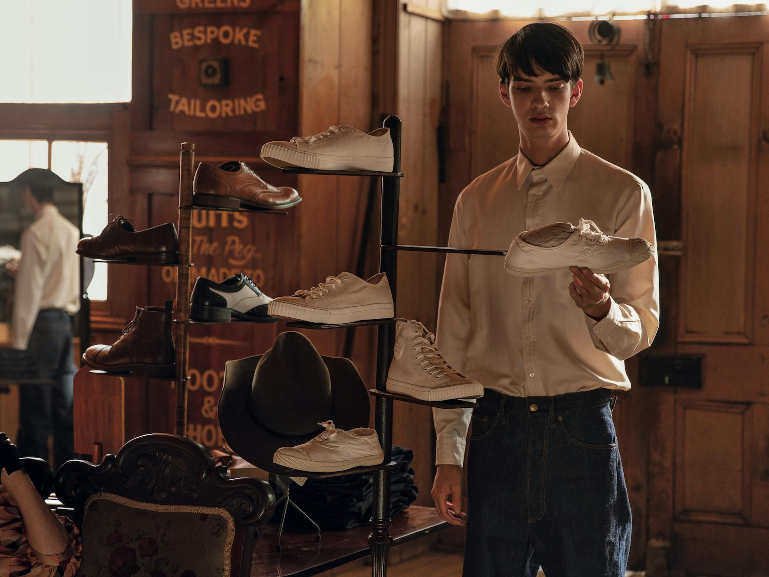 Peter Gordon (Kodi Smit-McPhee) examines a shoe on a rack in a wood paneled store.