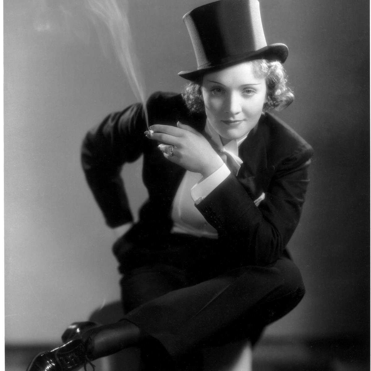 Marlene Dietrich in Morocco wears a suit and top hat, and smokes a cigarette.