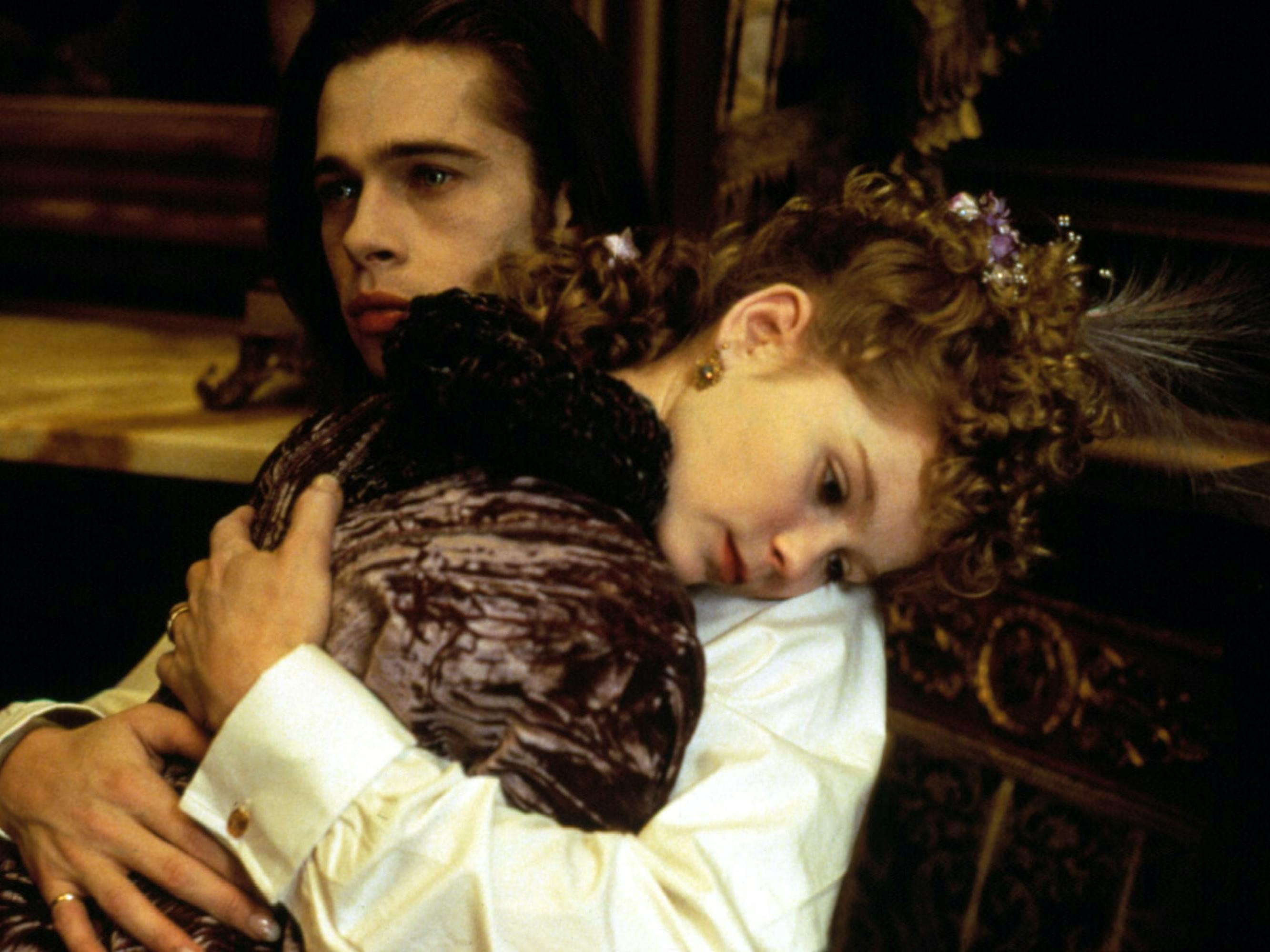 Louis (Brad Pitt) wears a white shirt and holds Claudia (Kirsten Dunst) who wears a dark velvet shirt and a headpiece.