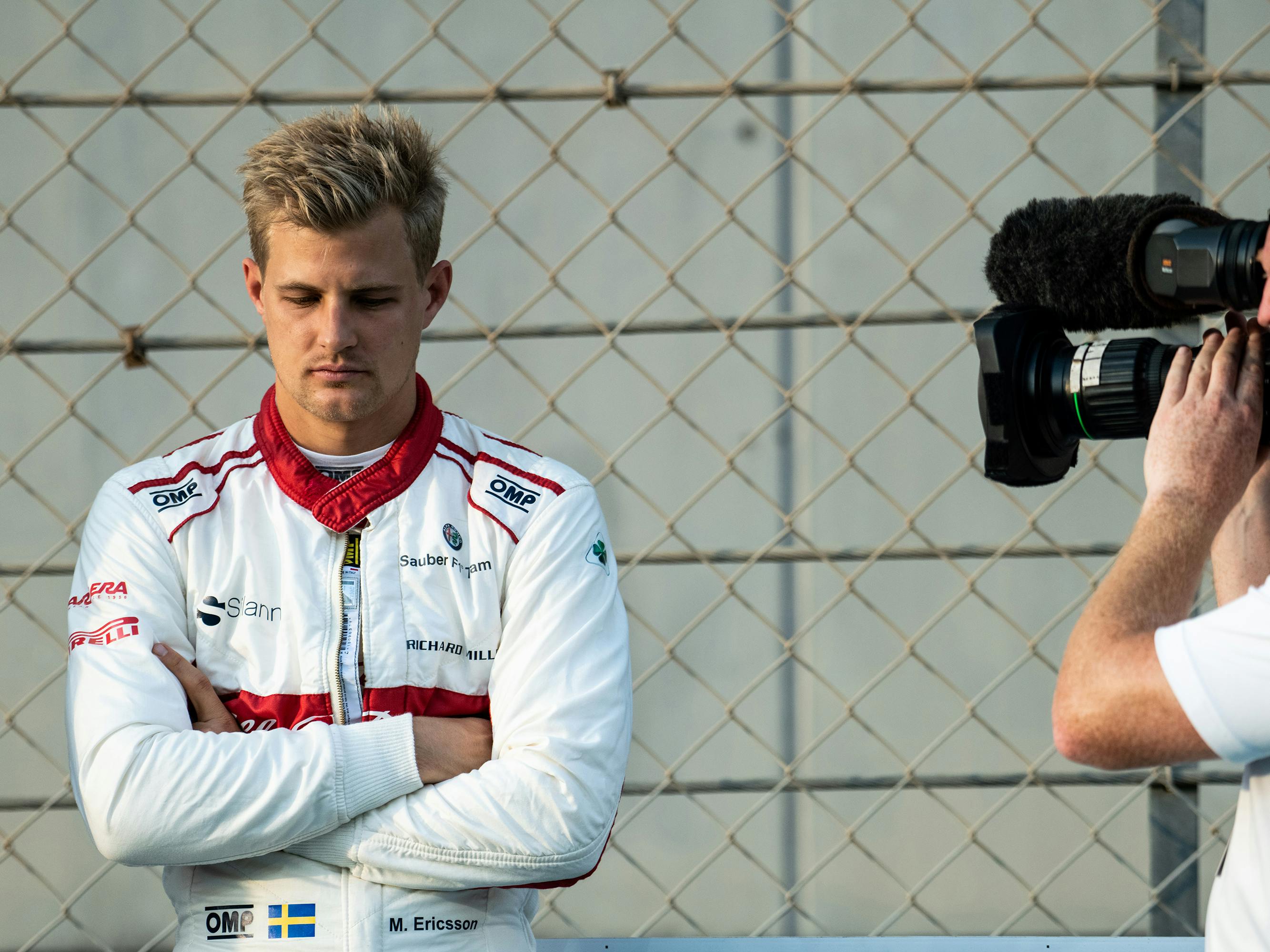 Marcus Ericsson wears a white-and-red sponsored shirt and looks grim. Don’t be sad — you’re on camera!