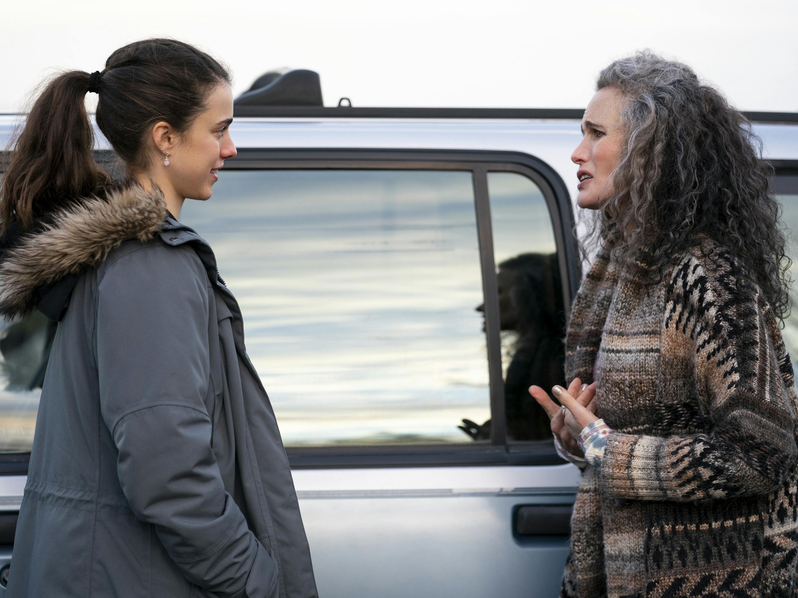 Alex Russell (Margaret Qualley) and Paula (Andie MacDowell) stand by a silver car. Russell wears a navy parka, and MacDowell wears a patterned sweater.