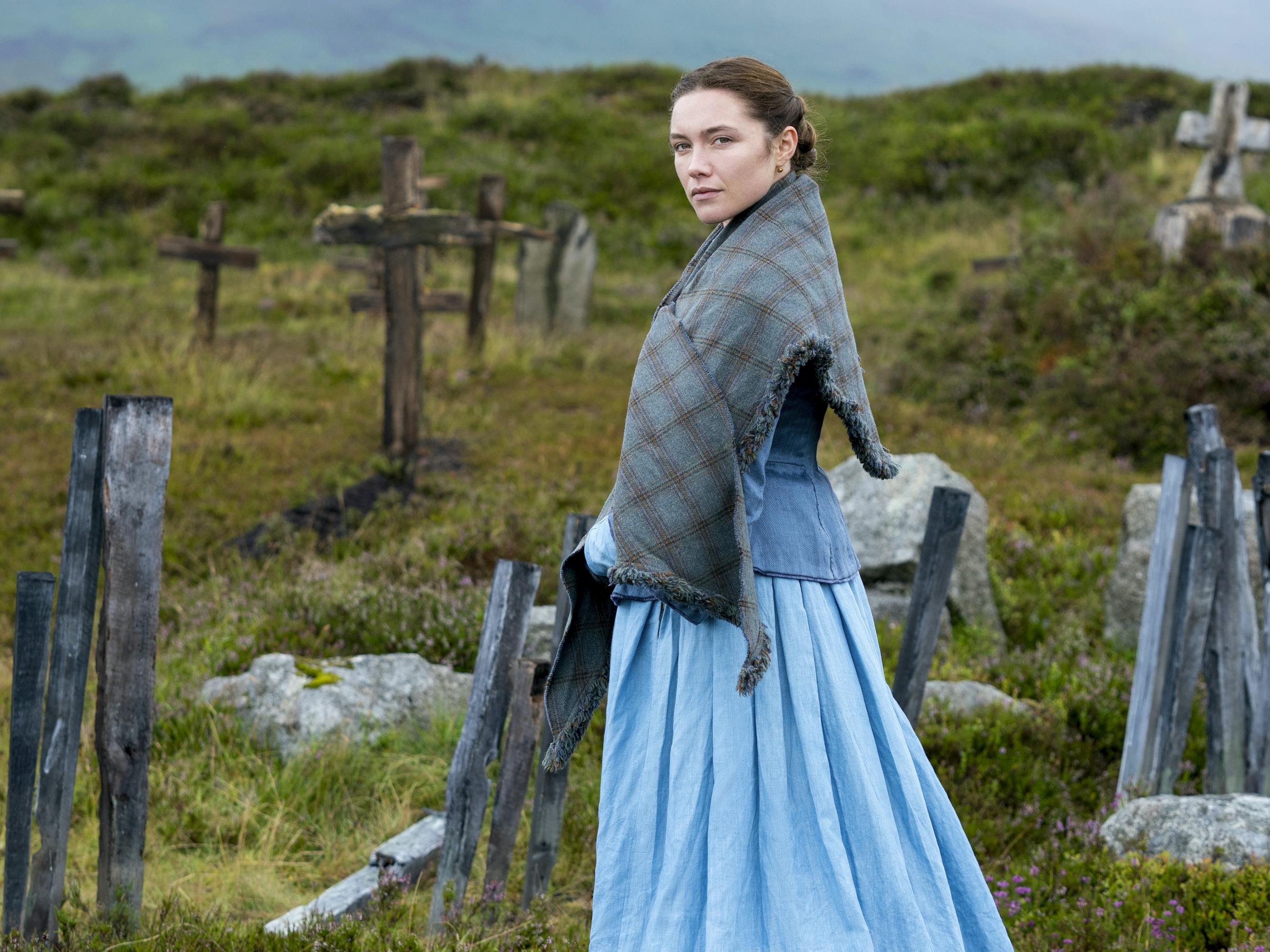 Lib Wright (Florence Pugh) wears a blue dress and stands in a foggy cemetery dotted with crosses.
