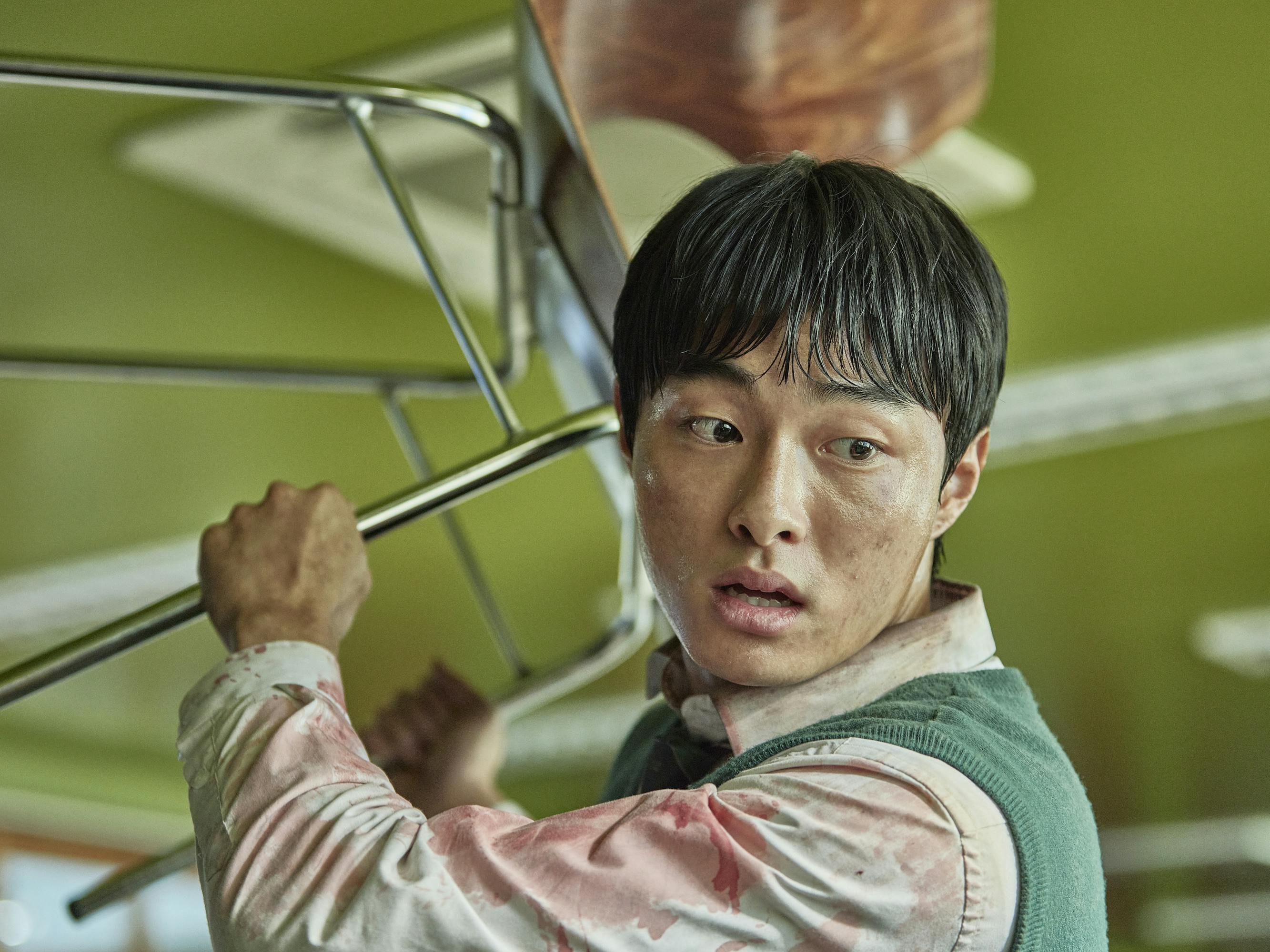 Yoon Chan-young in All of Us Are Dead brandishes a chair in a green-painted room.
