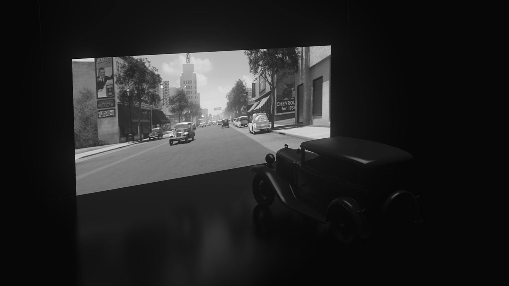 A 1930’s era car sits facing a screen, showing the rendered streets of Wilshire Blvd made to replicate that time in Hollywood. 