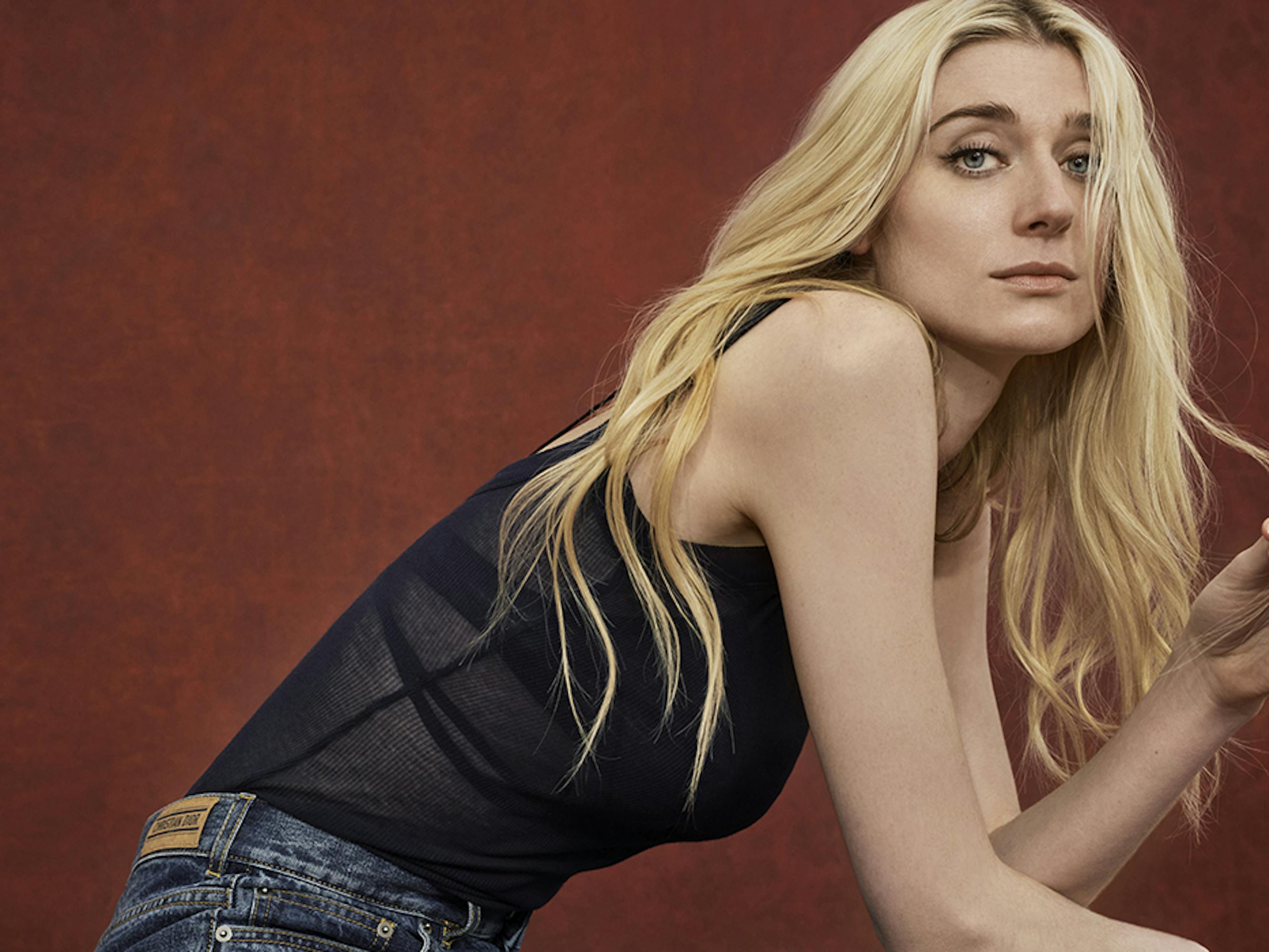 Elizabeth Debicki wears a black tank top and jeans and fiddles with her long blond hair. 