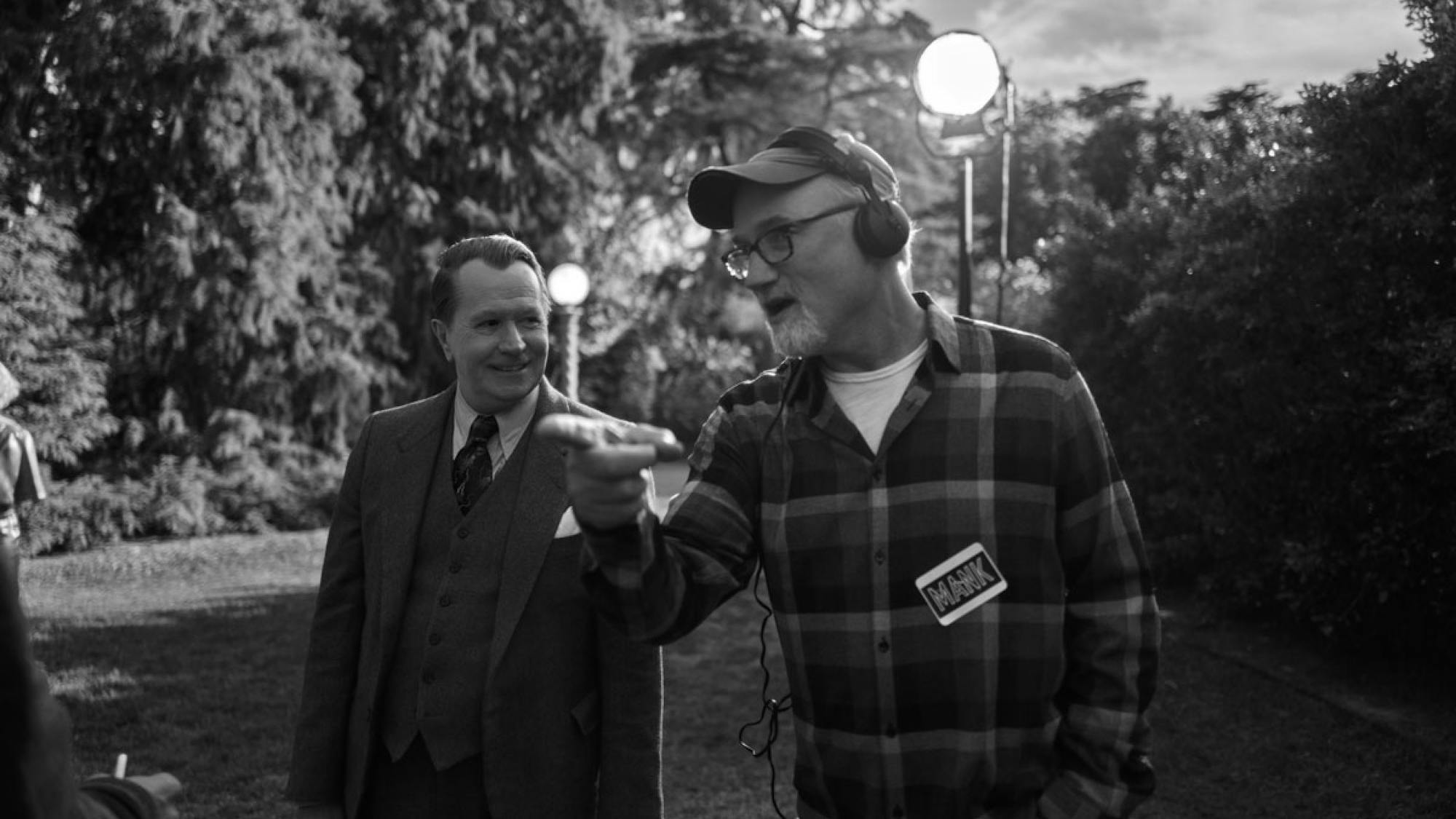 Fincher directs Oldman on the San Simeon set. Oldman is in costume in a suit, while Fincher sports headphones and a flannel shirt on which he’s stuck a sticker reading “Mank.”