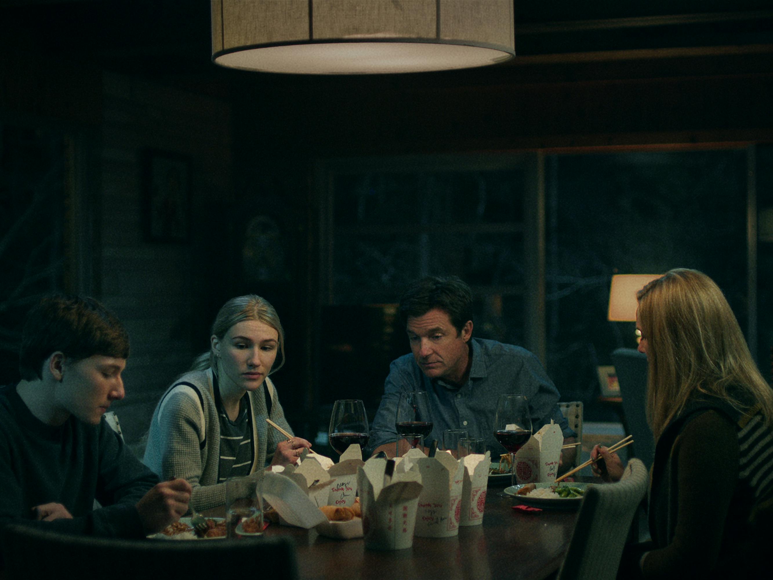 Skylar Gaertner, Sofia Hublitz, Jason Bateman, and Laura Linney sit around a dinner table filled with Chinese takeout.  