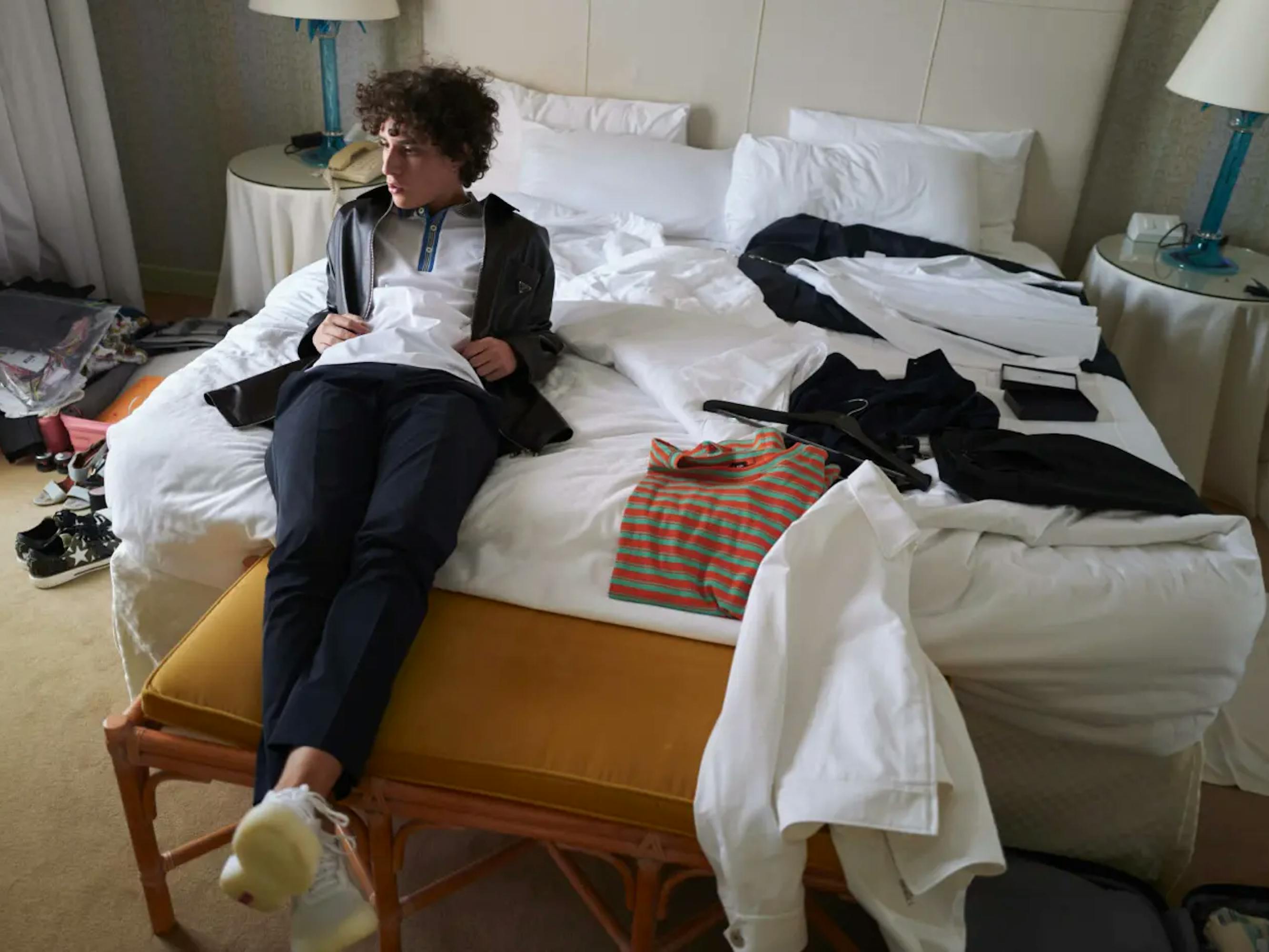 Filippo Scotti wears part of a suit as he reclines on a white bed. There are clothes strewn about on the mattress and floor, and he looks absentmindedly off to the side. If it weren’t for the tux and imminent Venice film festival award, he would seem like a regular teenage boy.